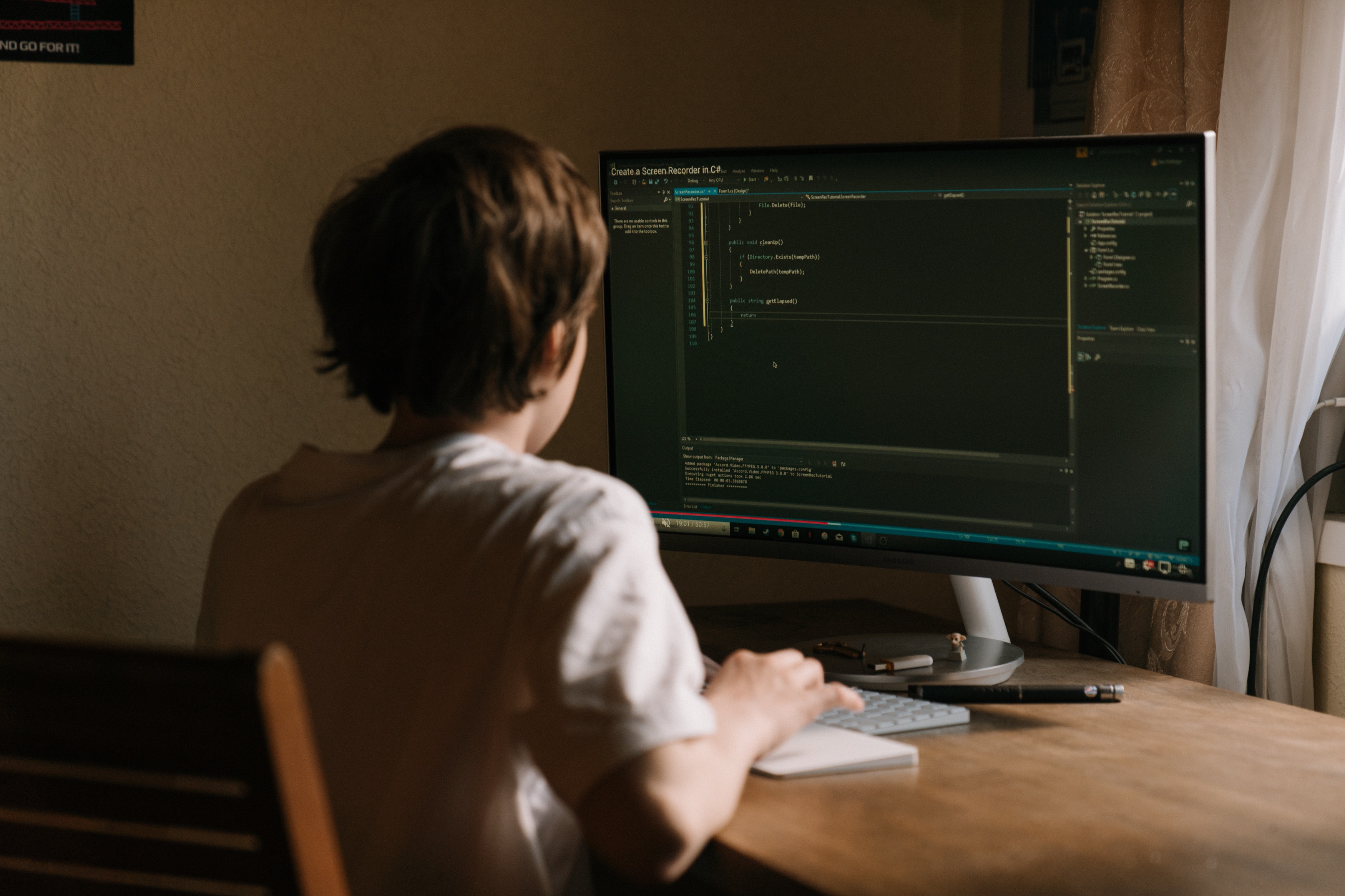 A person sitting at a desk in a home office looking at a screen showing code