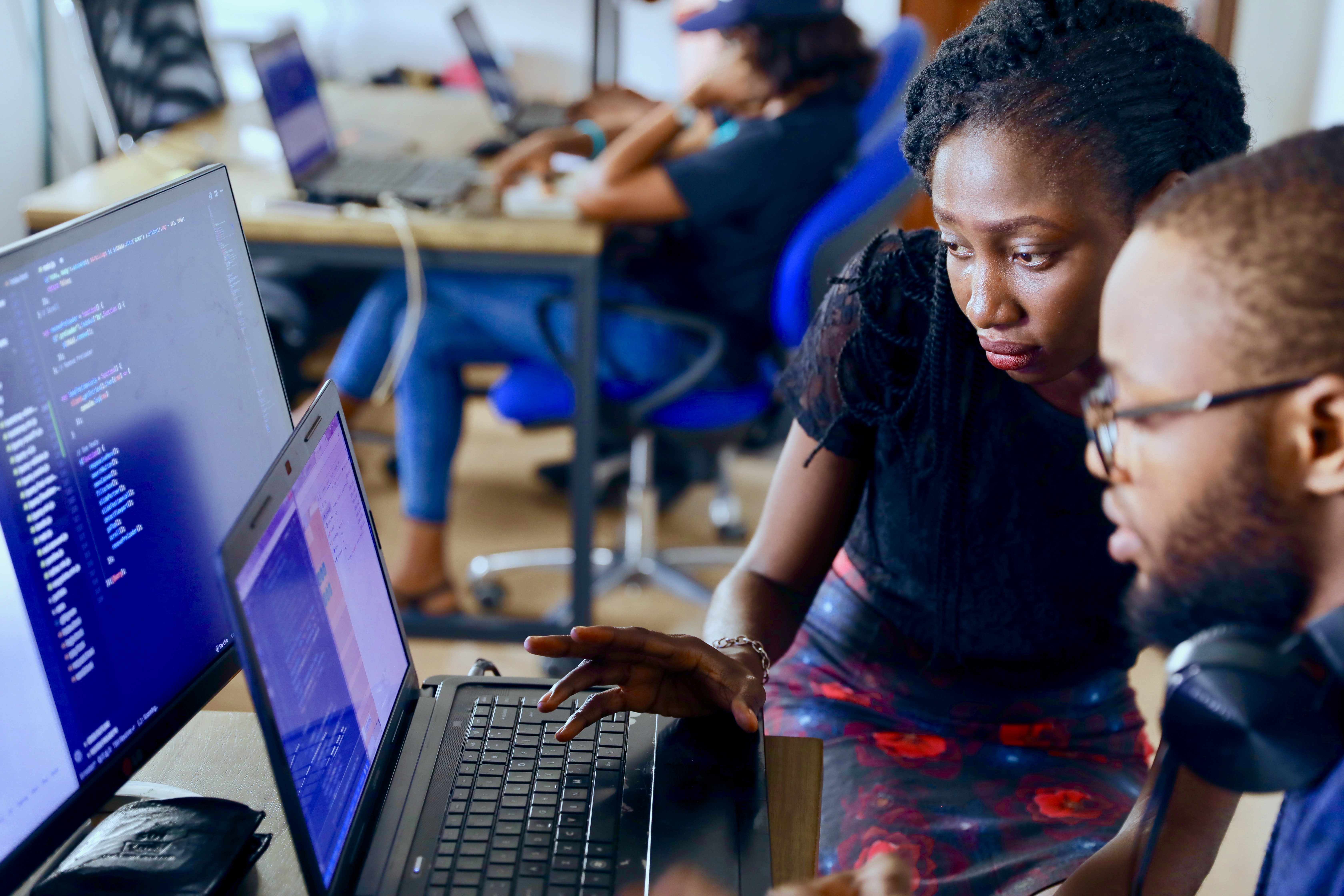 Two people at a desk looking at a laptop and monitor