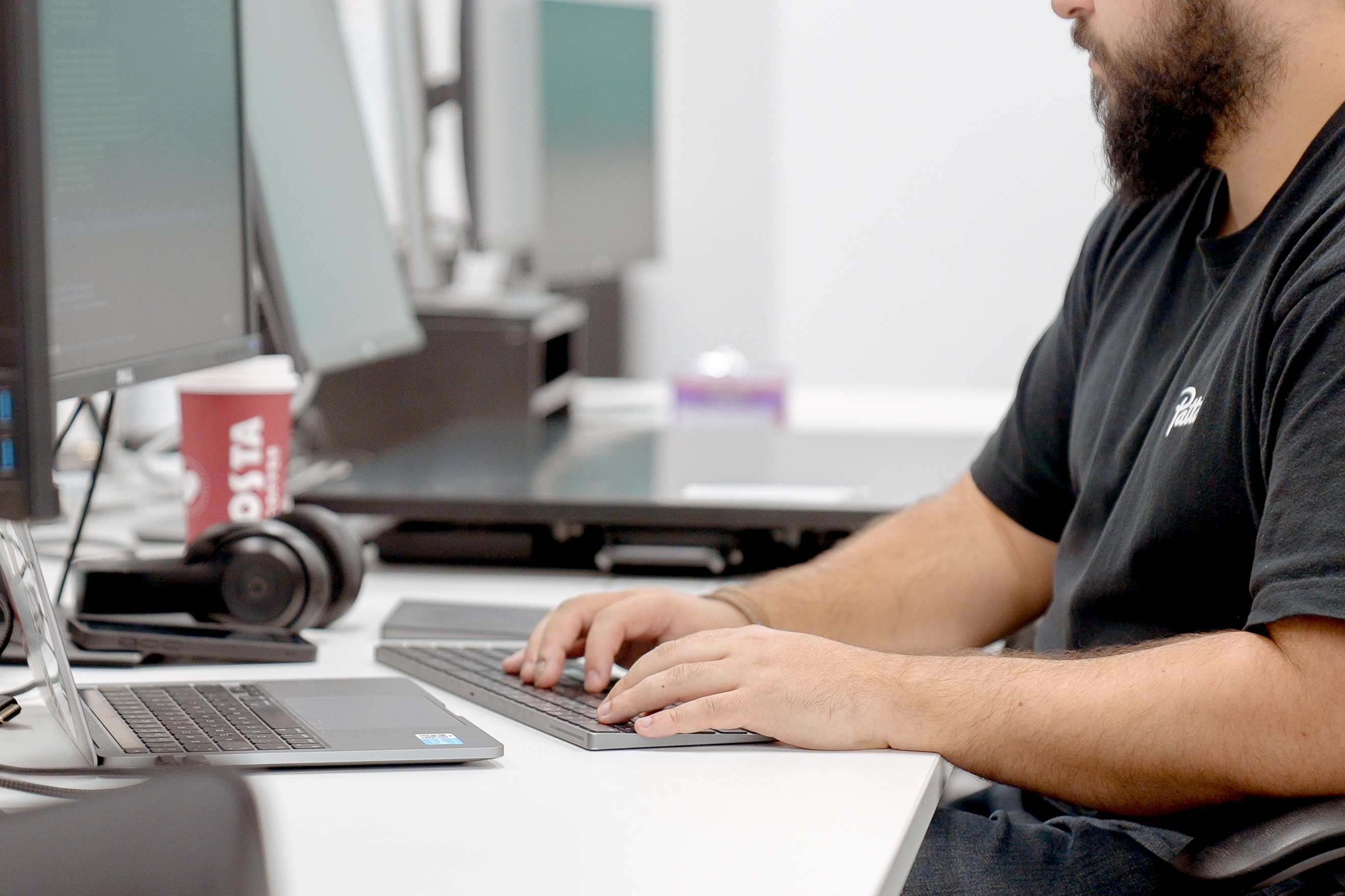 A man in a black t-shirt sitting at a desk typing on a keyboard