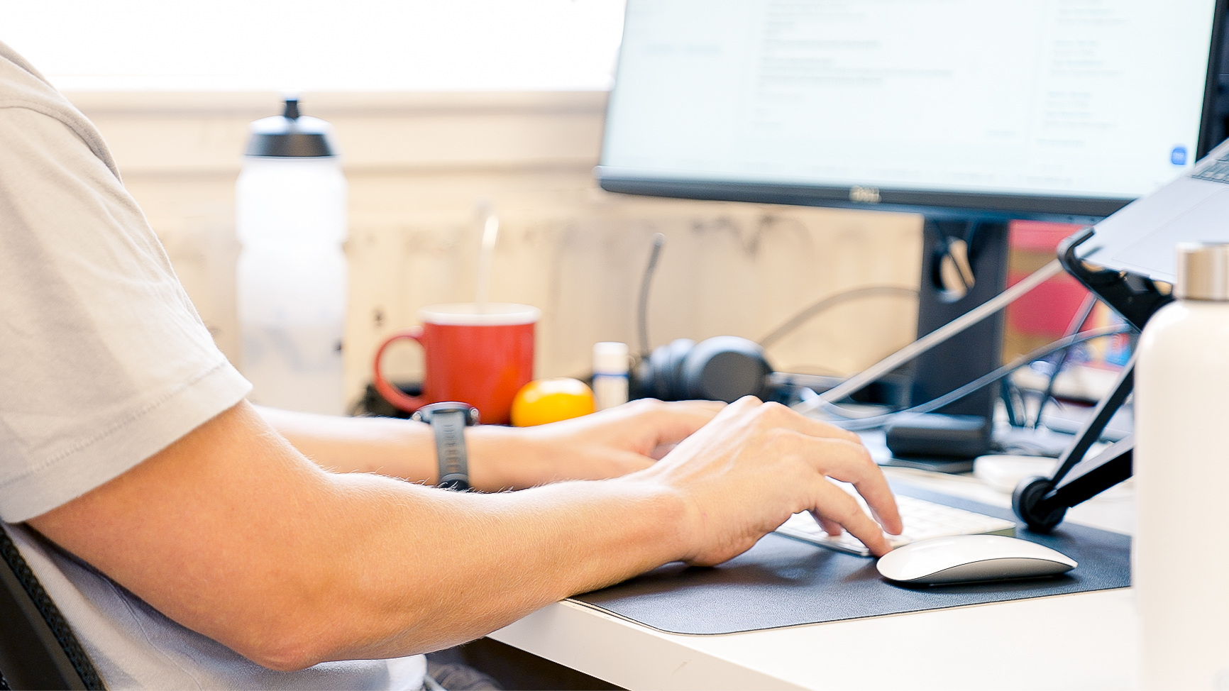 The arms of someone typing at a desk are seen from the side and slightly behind