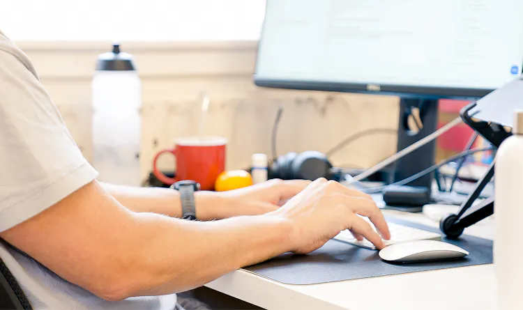 The arms of someone typing at a desk are seen from the side and slightly behind