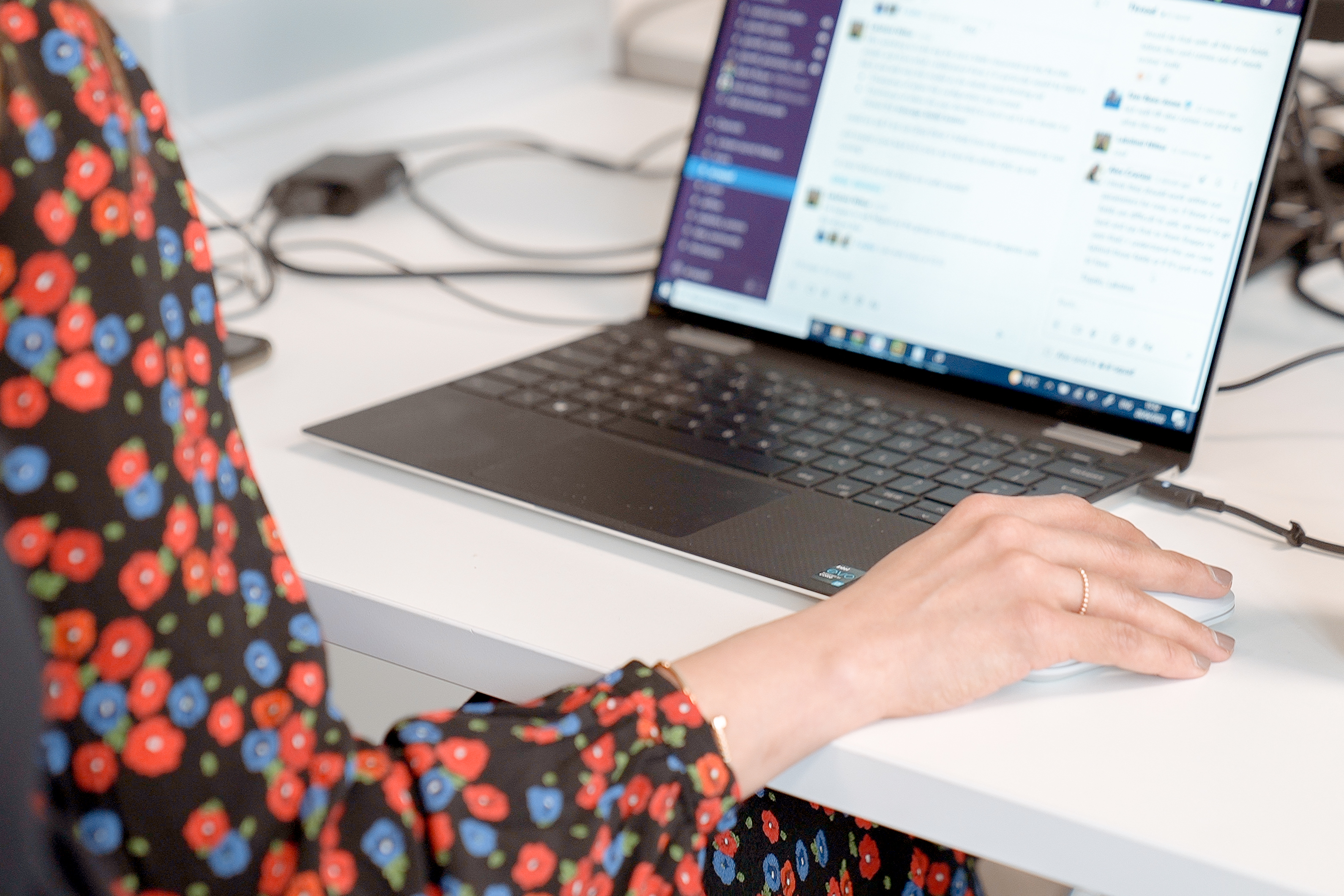 Cover of A laptop is on top of a desk, with the arm of a person wearing a flowery dress working at it seen from behind article