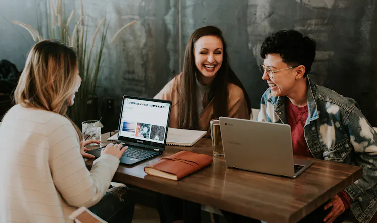 Three women sitting around a desk working on laptops