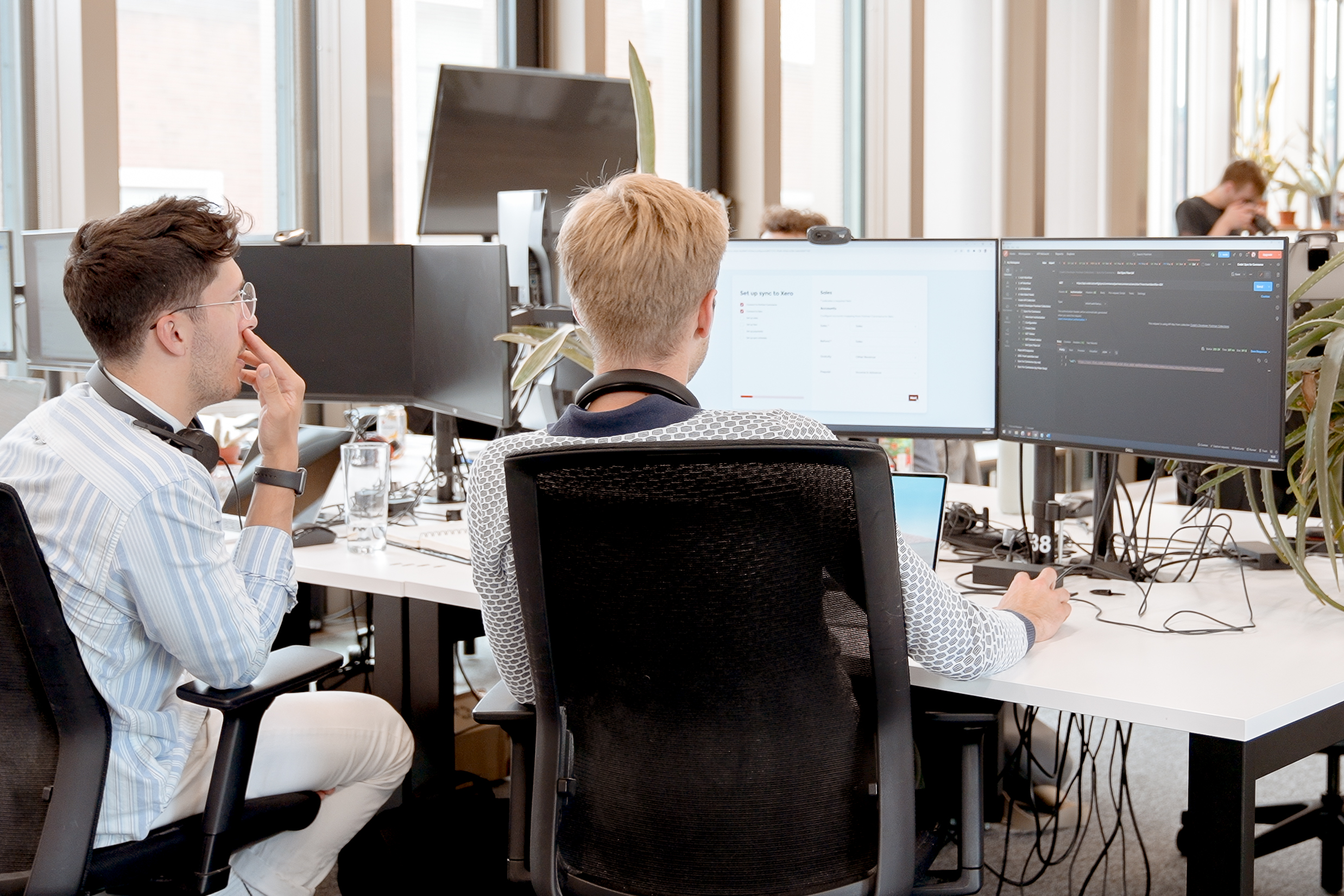 Cover of Two people sitting in an office looking at code on monitors article