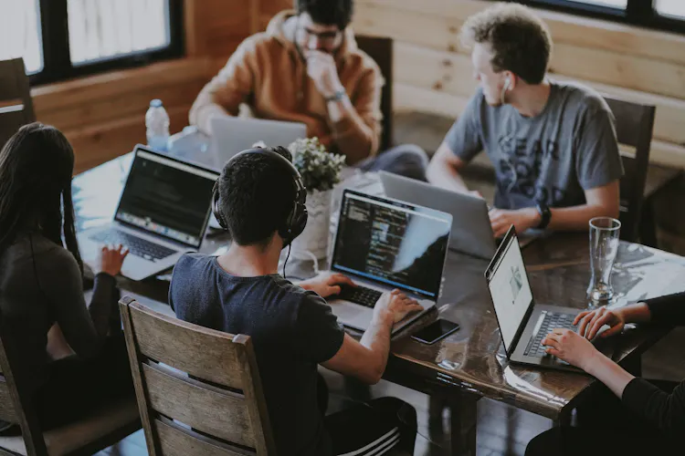 Cover of Four people sitting around a desk working on laptops article
