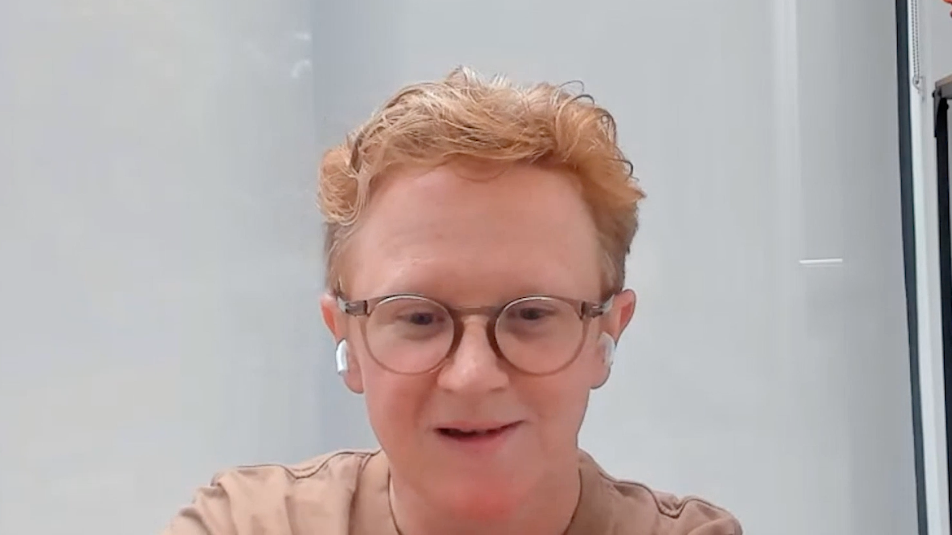 Person with glasses smiles in front of computer