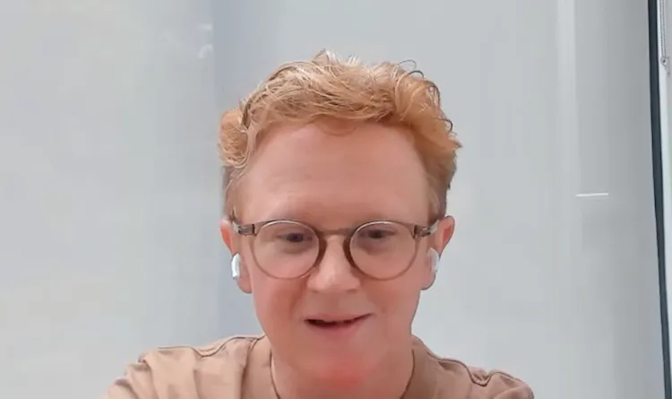 Person with glasses smiles in front of computer
