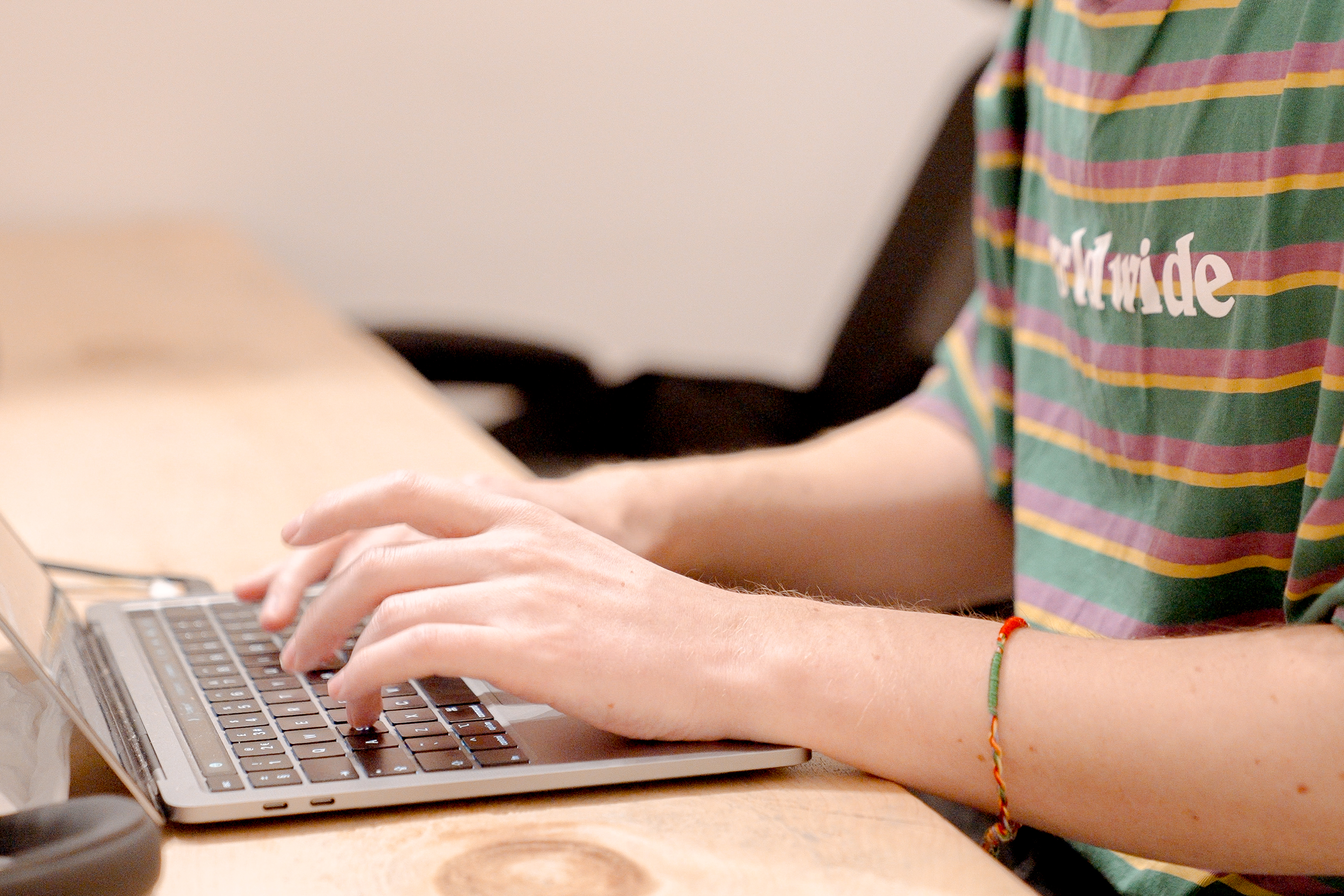 The hands and forearms of someone wearing a green t-shirt working at a laptop