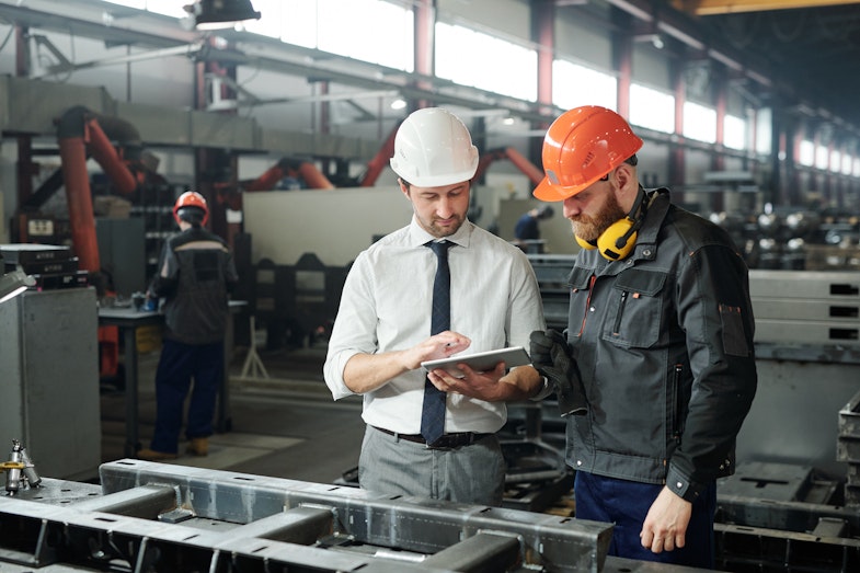 Two men standing in a factory with safety helmets