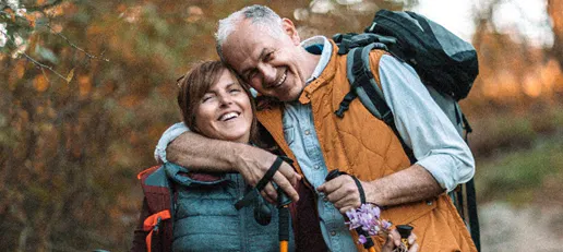 An active senior couple embracing and laughing while hiking outdoors on a trail