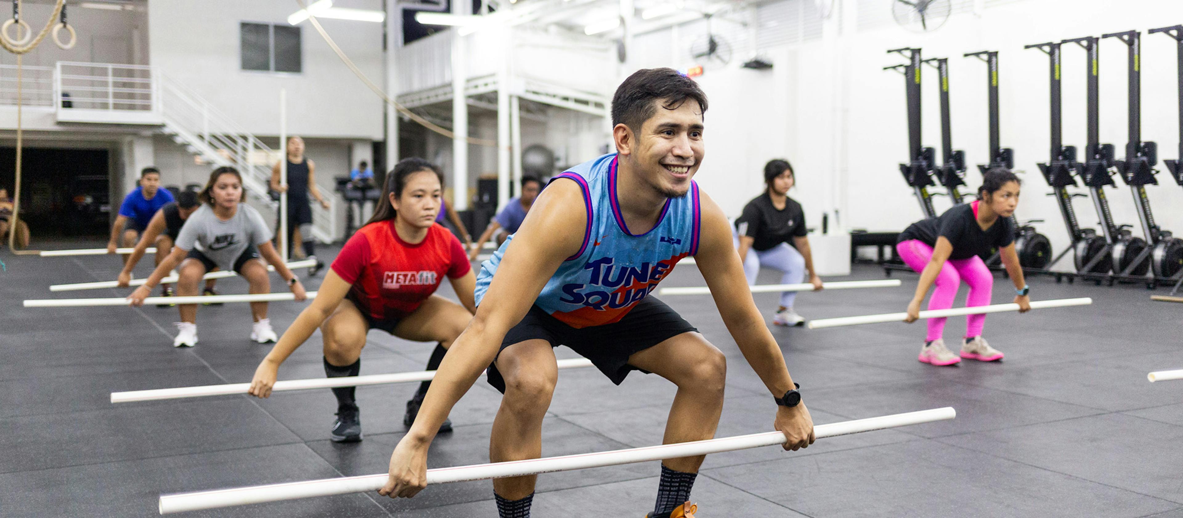 A group of people at the gym holding a bar while squatting