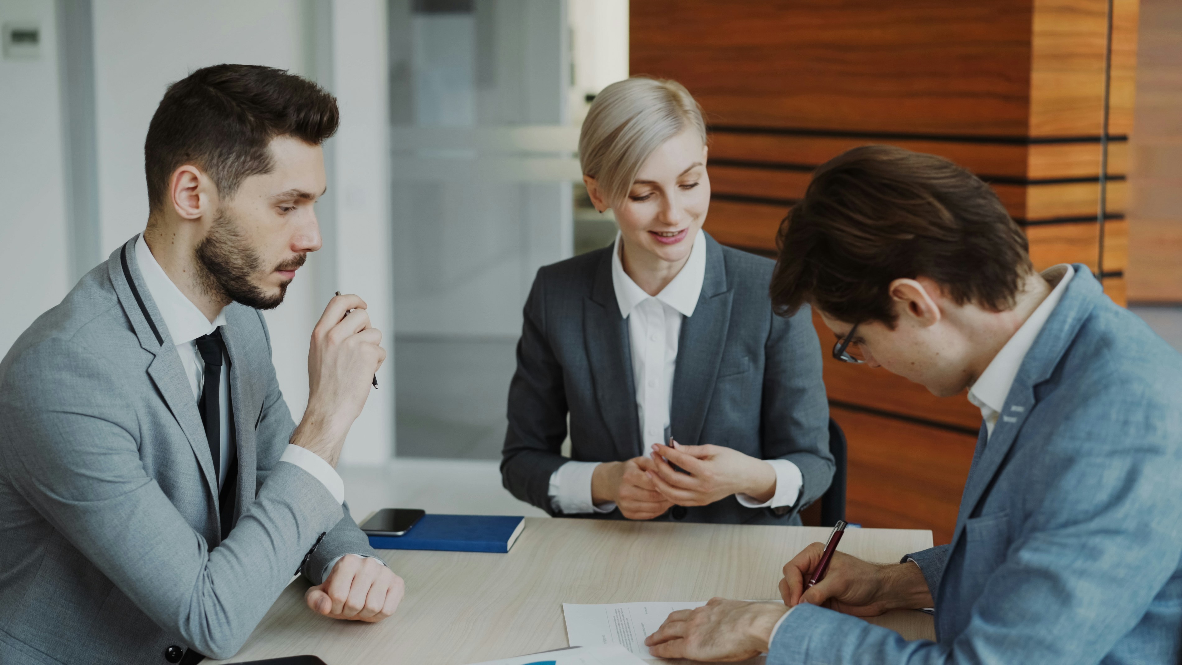 Three people sitting around a table, one is signing a contract