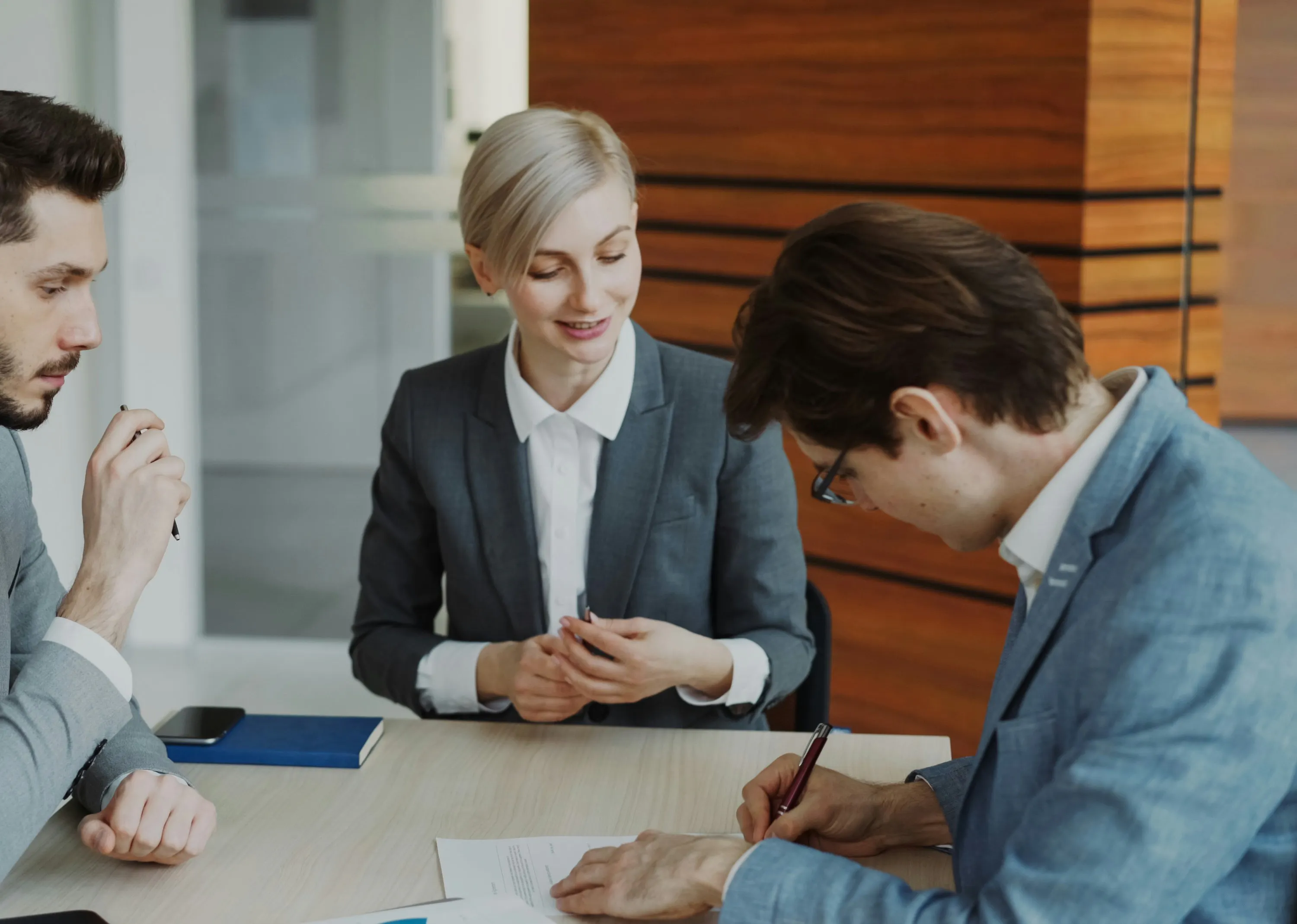 Three people sitting around a table, one is signing a contract