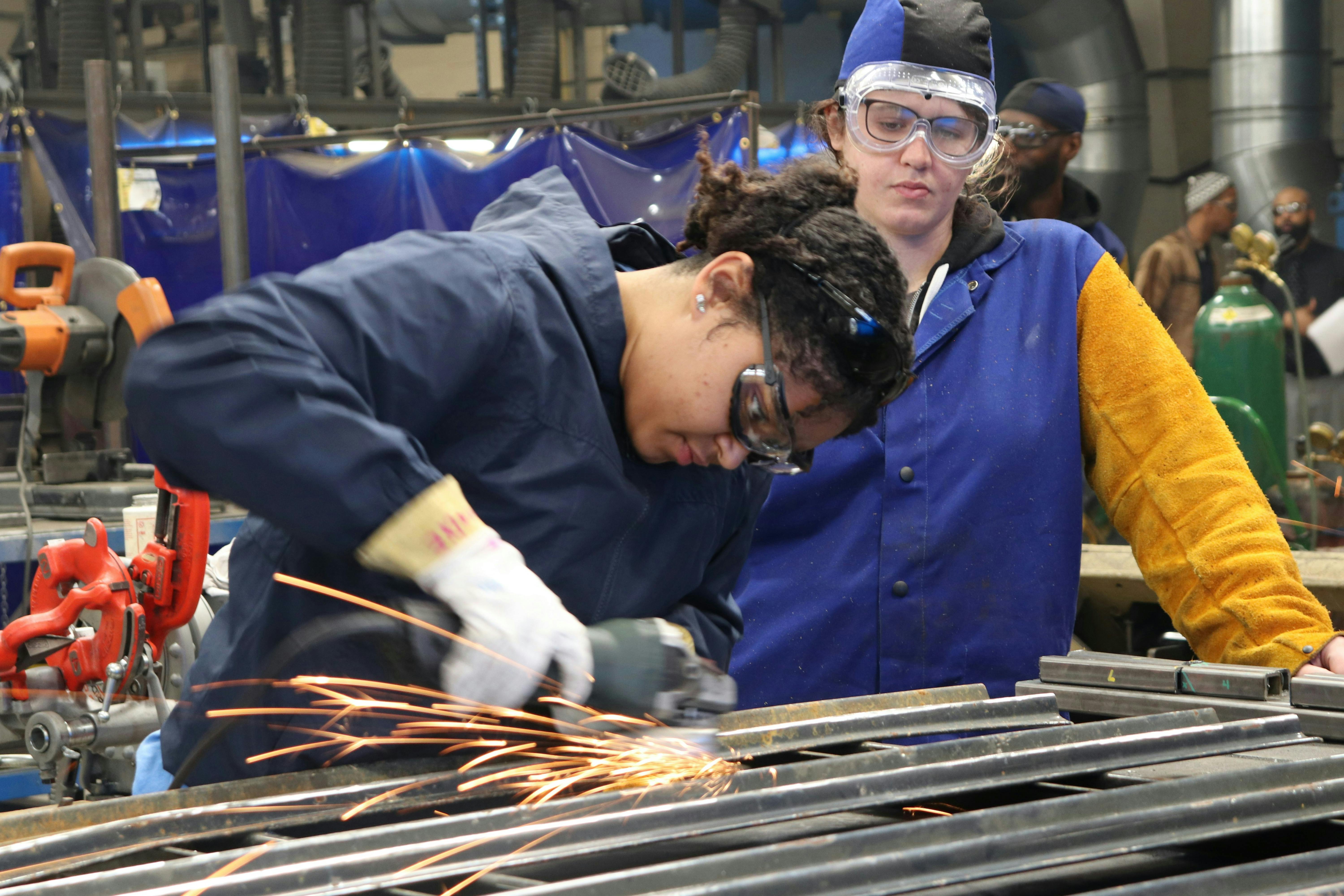 Two women in a factory using a tool to cut metal