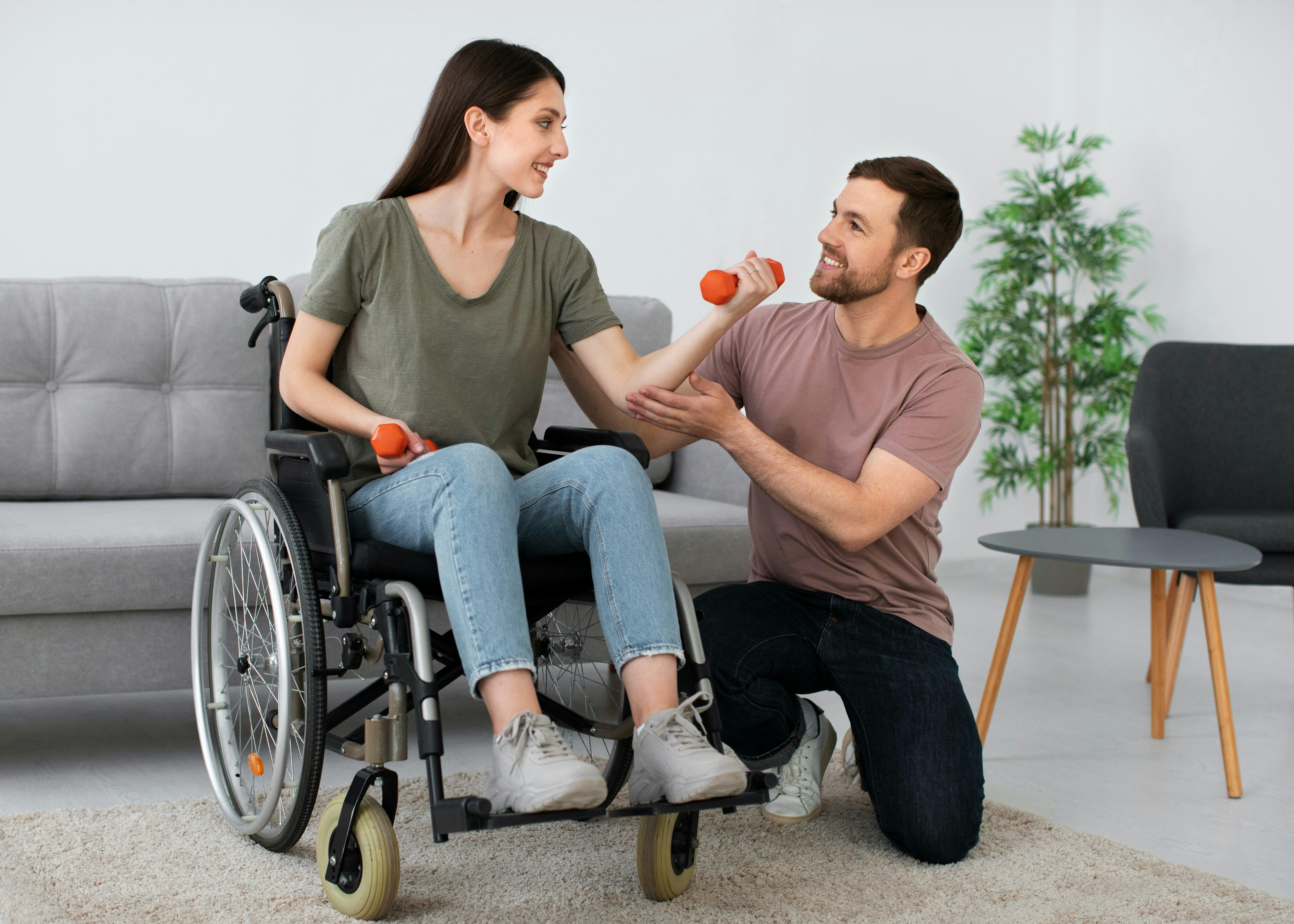 Woman in wheel chair lifting arm weights with man next to her helping
