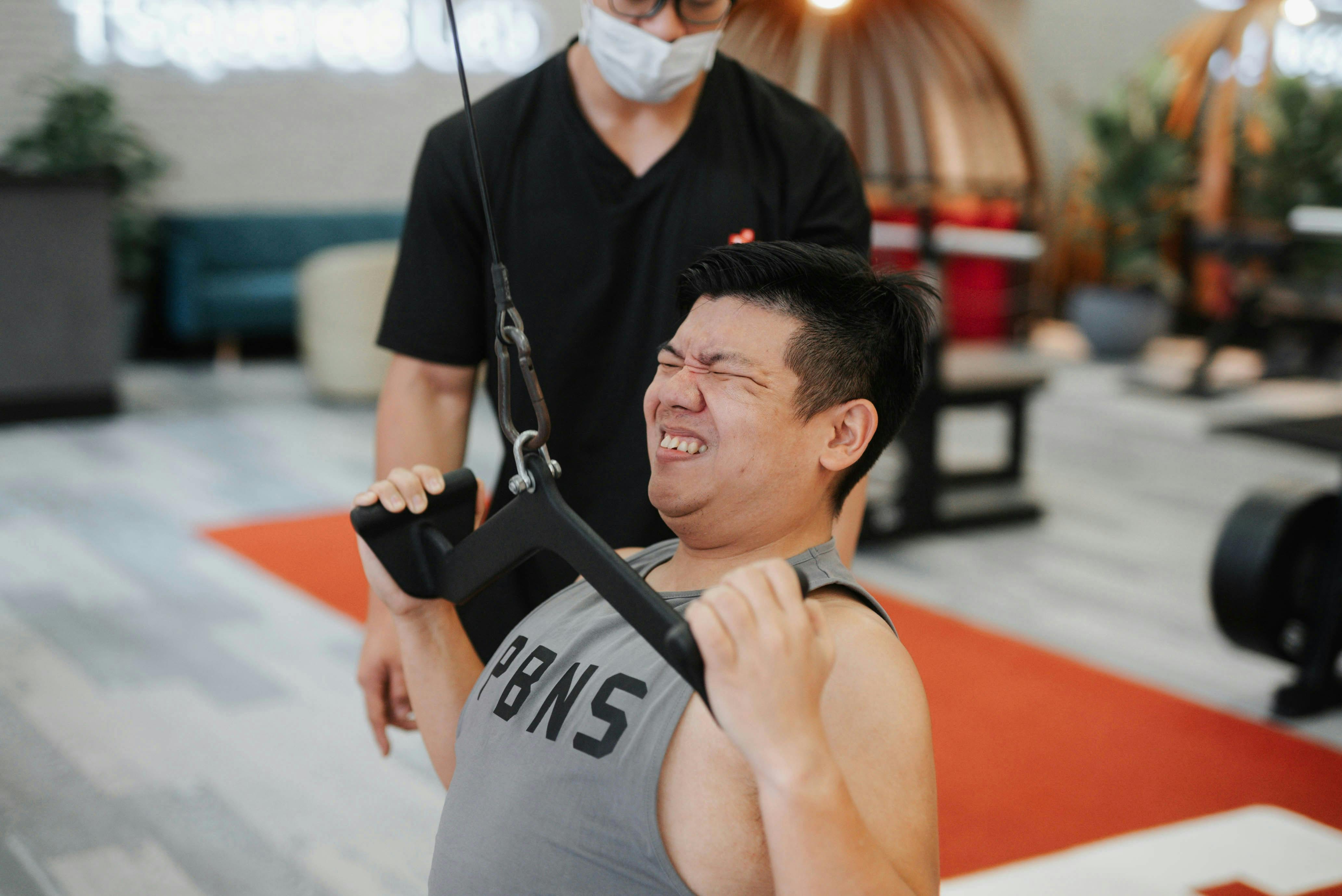 Man using arm weight machine with assistant behind him