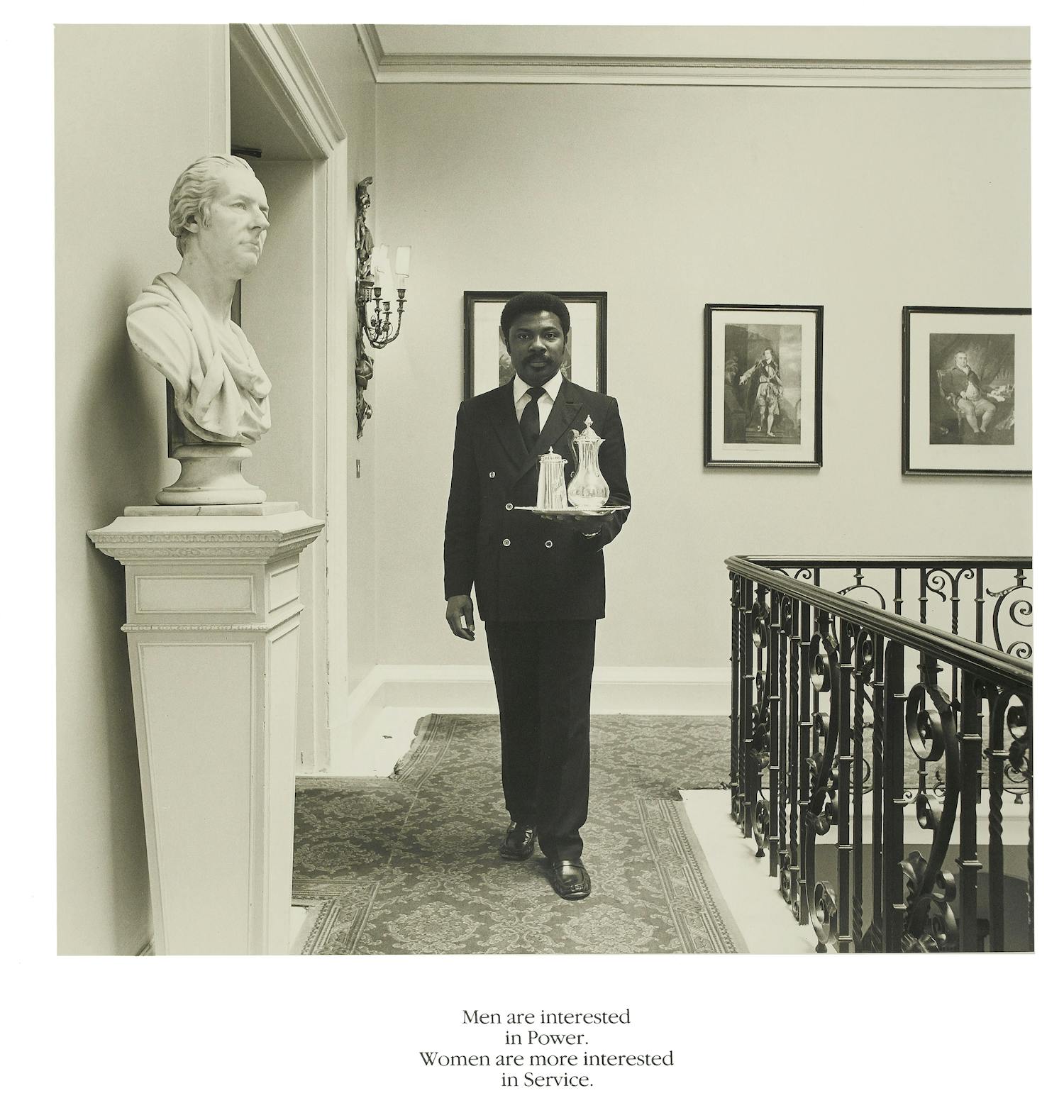 [ID: The first image shows a photograph of a man walking through a hallway towards the camera. He is carrying a tableau with two carafes on it. On the left side of the image is a marble bust of a man, looking to the top right corner of the image. End of ID]