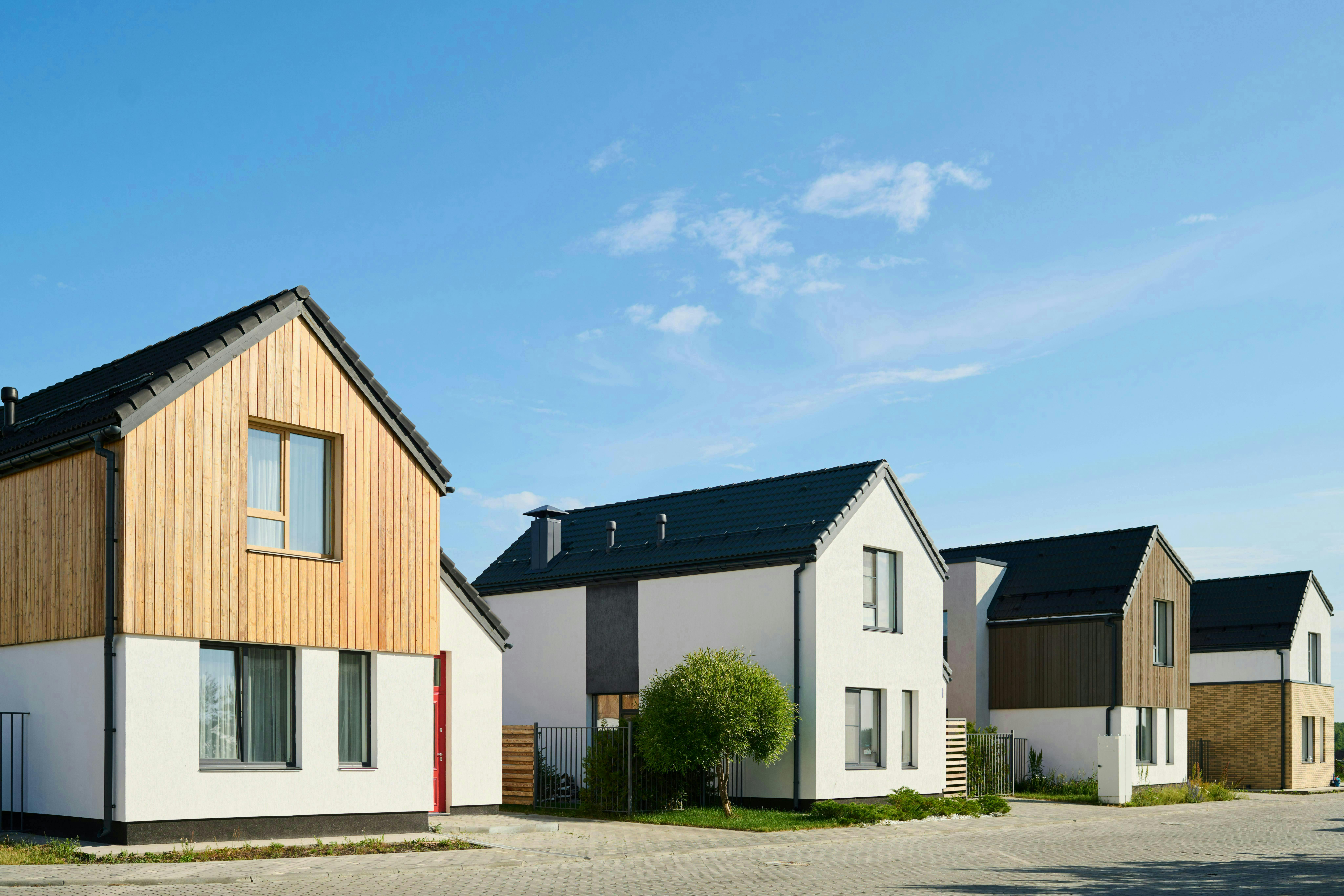 Perspective view of several small houses standing in row in rural environment against blue sky on sunny day showcasing passivhaus