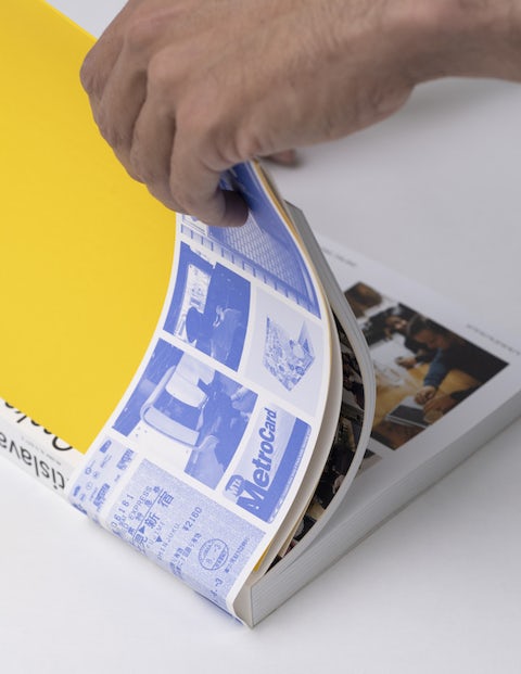 Hand flipping through the pages of 'Around the World in 250 Coworking Spaces,' showcasing the blue and white interior design.