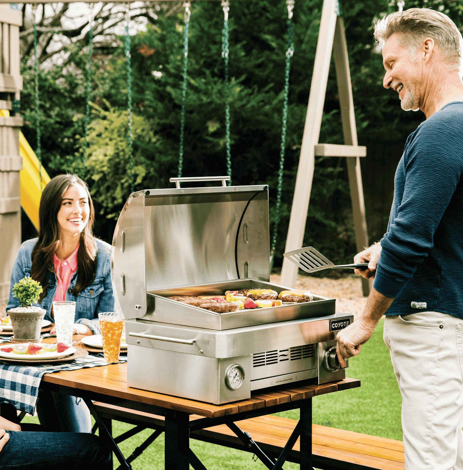 family cooking on coyote portable grill in their backyard