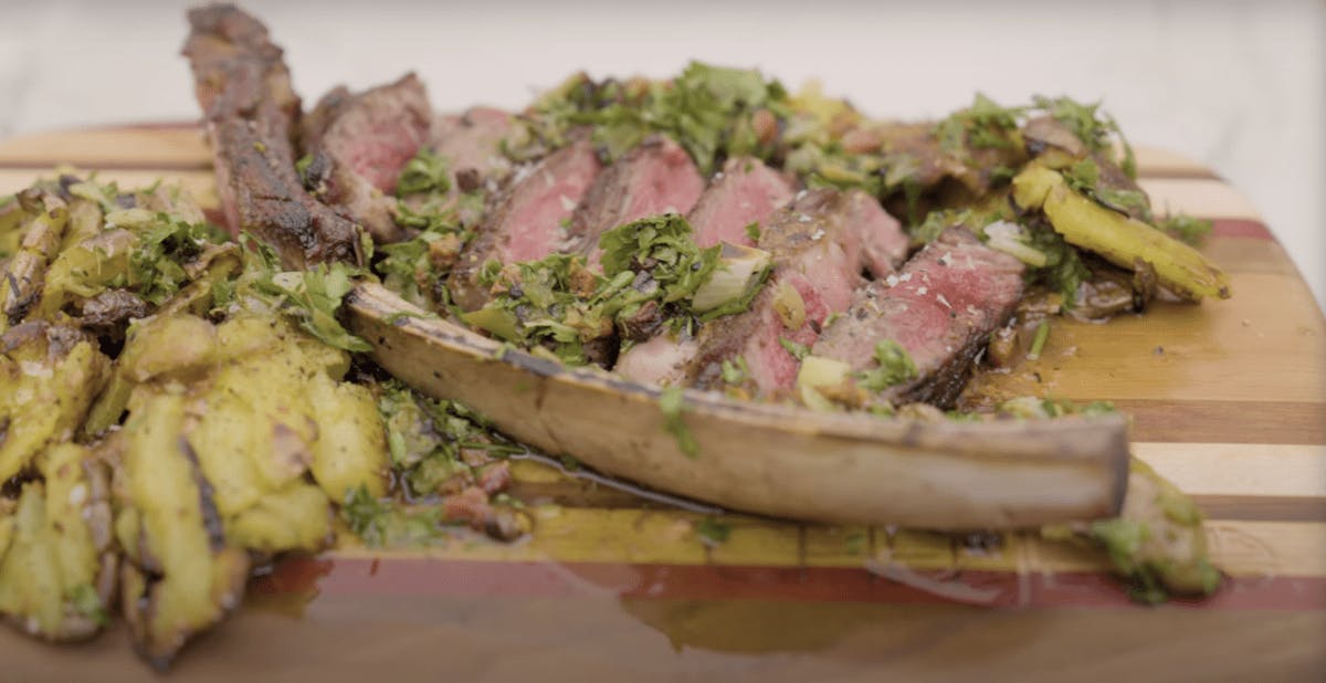 Juicy tomahawk steak off the bone with smashed potatoes and herb sauce on a wood cutting board