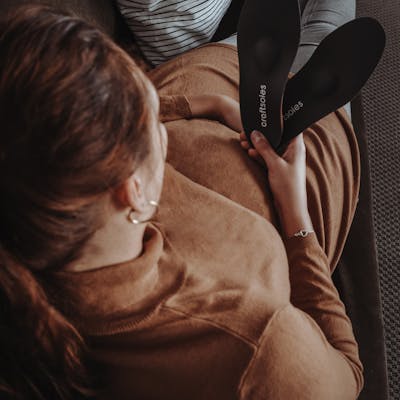 Schwangere Frau sitzt auf dem Sofa und schaut Einlagen an