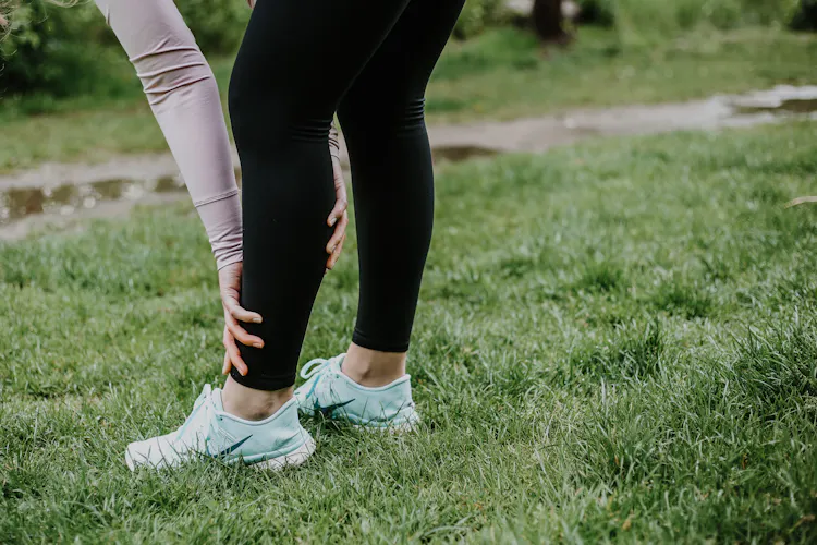 Frau greift sich an schmerzendes Schienbein