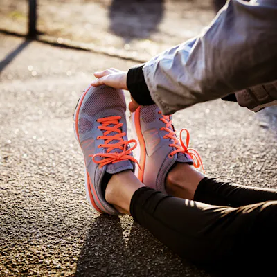 Frau sitz auf dem Boden und greift sich an die Sportschuhe