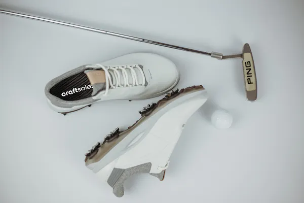 Golfschuhe mit Schläger und Ball vor weißem Hintergrund