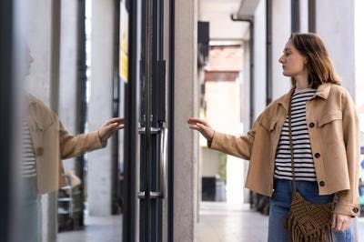 A woman reaches towards a glass external door of a building, as if she is about to enter.