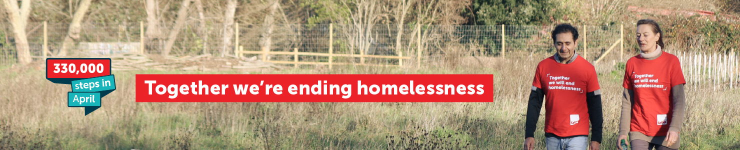 Two people wearing red Crisis t‑shirts walk together through a grassy park. A banner graphic on the left reads “330,000 steps in April,” and a large red message across the image says “Together we’re ending homelessness.”