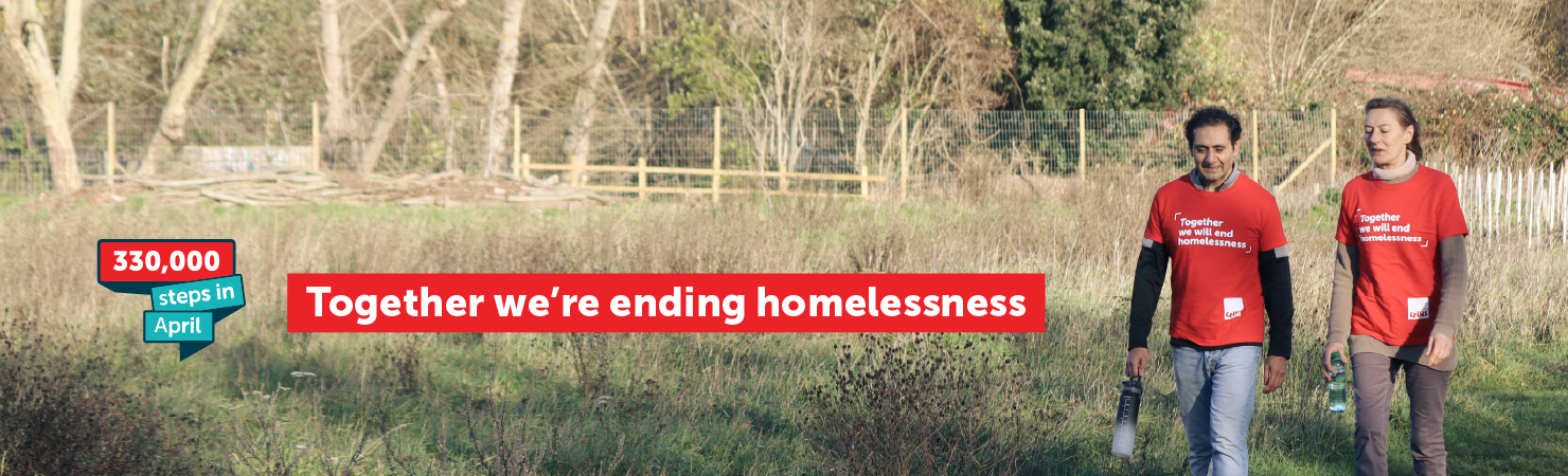 Two people wearing red Crisis t‑shirts walk together through a grassy park. A banner graphic on the left reads “330,000 steps in April,” and a large red message across the image says “Together we’re ending homelessness.”