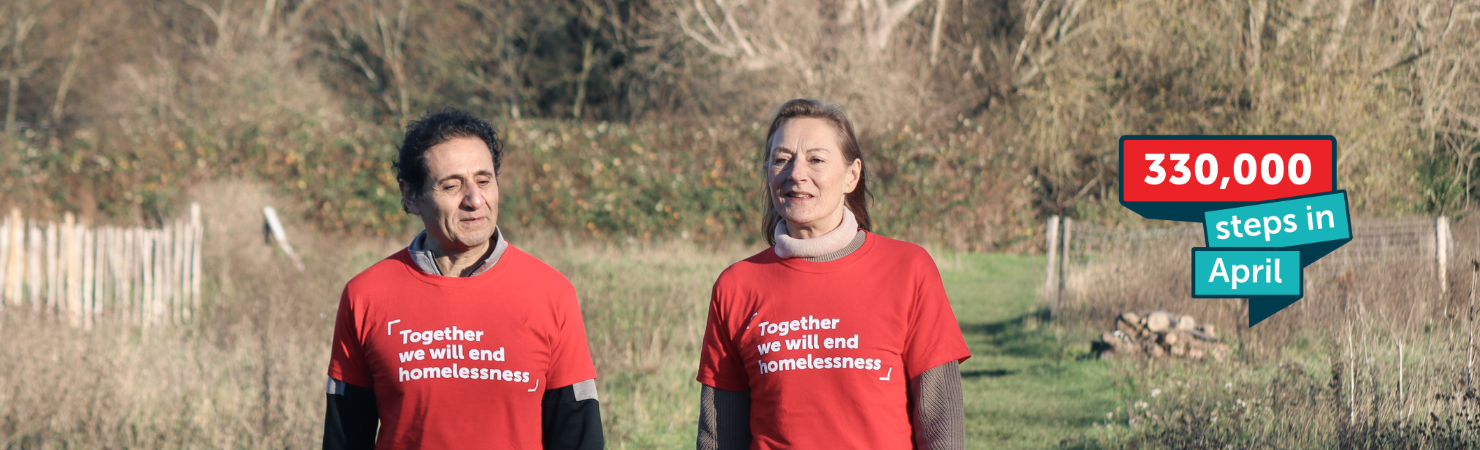A man and woman walk side by side in a field, talking and wearing red Crisis t-shirts.