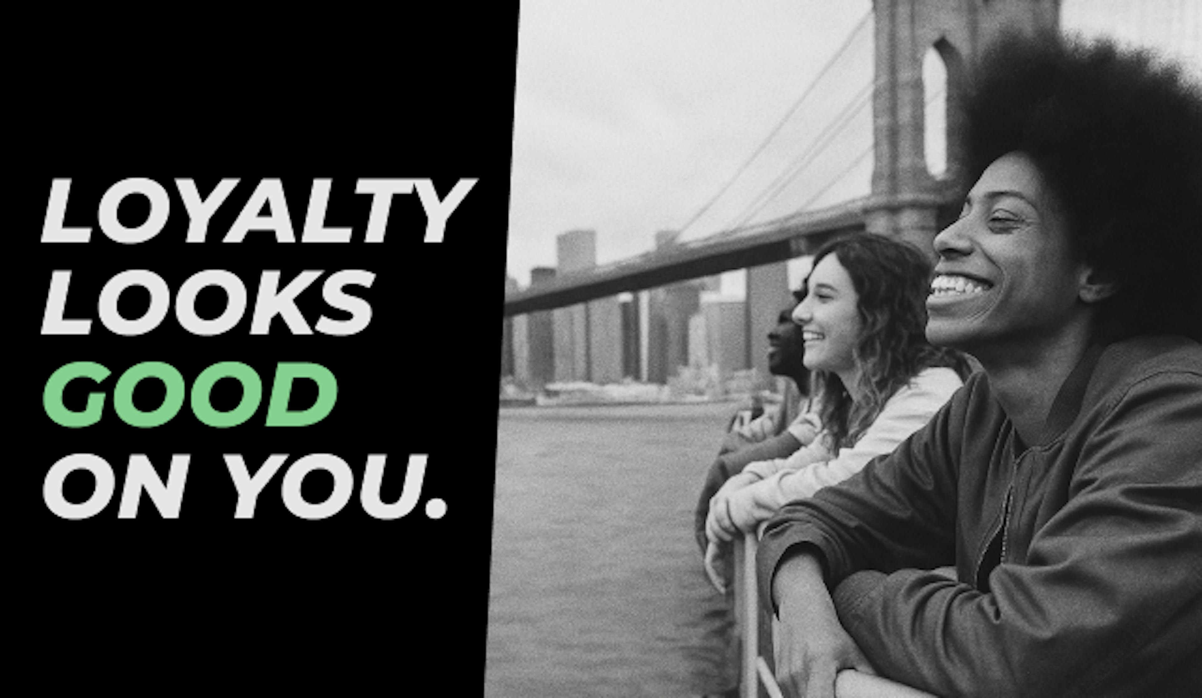 Black and white photo of three young people leaning on a railing by the waterfront, smiling and looking out toward the city skyline with the Brooklyn Bridge in the background. On the left, bold text reads: “LOYALTY LOOKS GOOD ON YOU,” with “GOOD” highlighted in green.