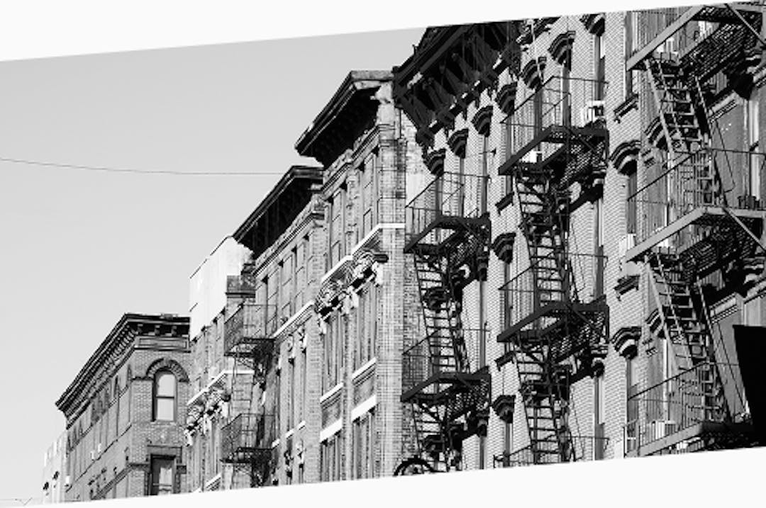 Angled view of historic apartment buildings in the Lower East Side of New York City, with rows of fire escapes casting strong shadows.