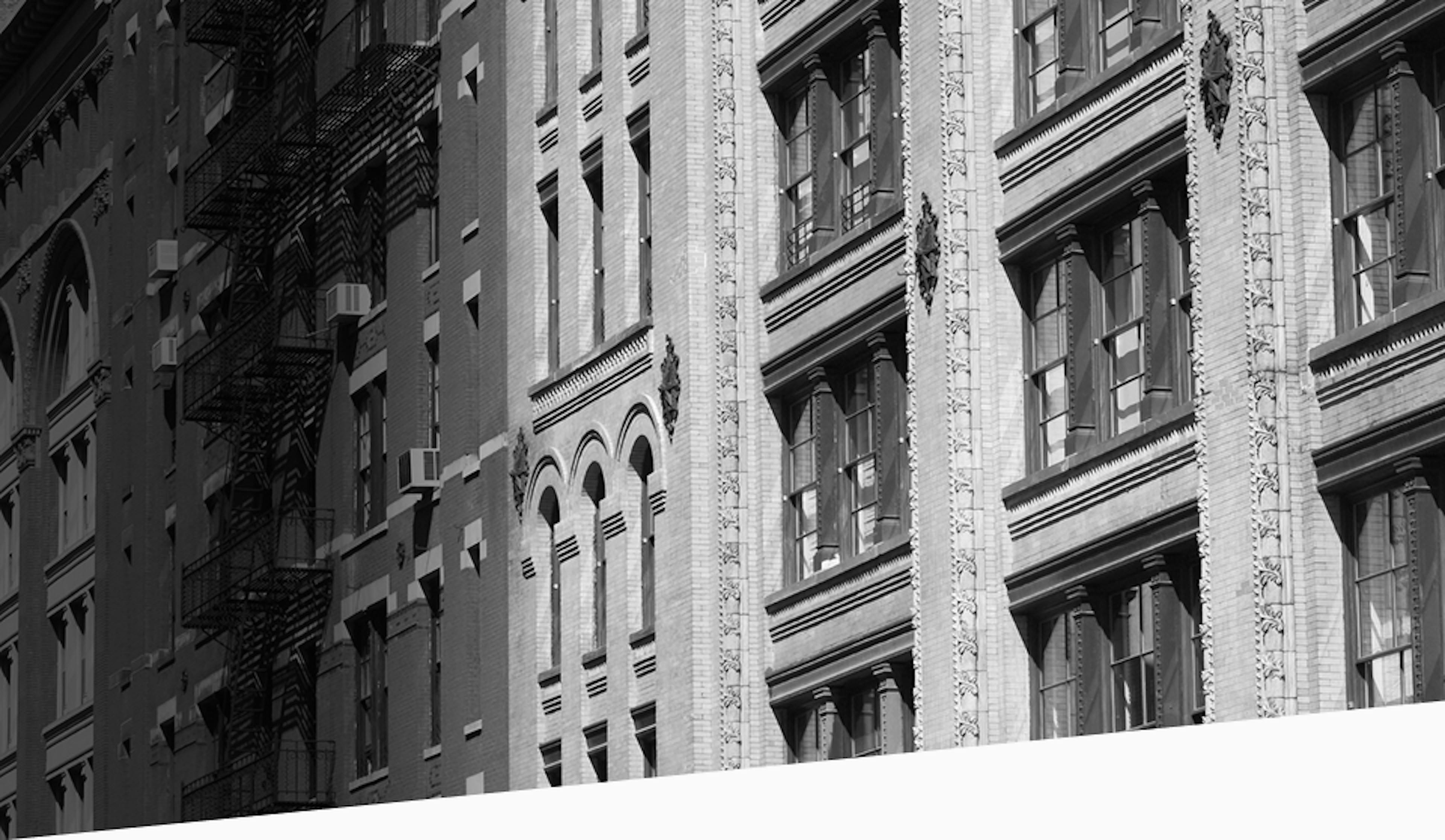 Black and white photo of historic brick and stone building facades in New York City, with decorative molding and tall windows.