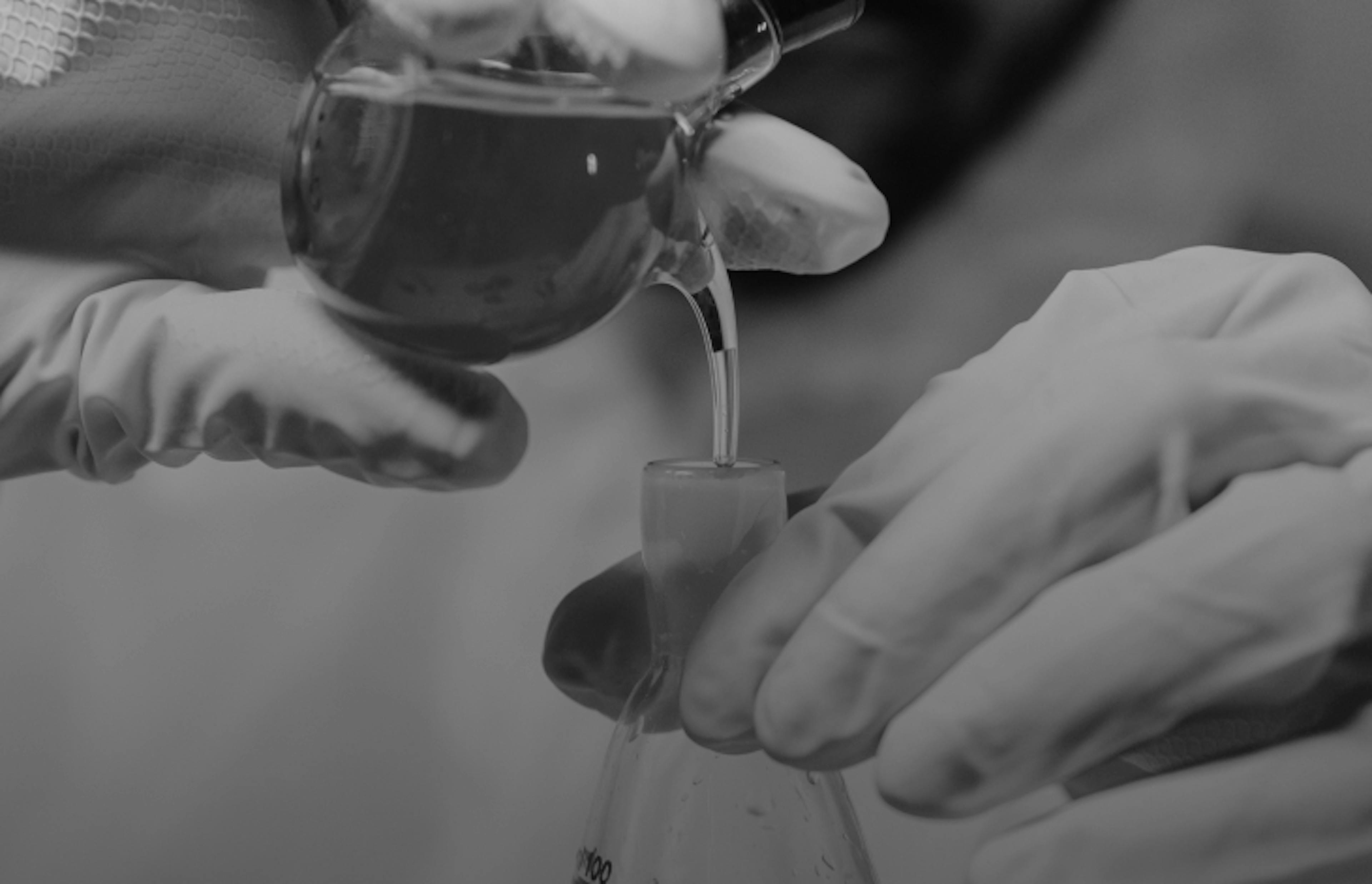 A lab technician wearing gloves and goggles pours cannabis oil into a beaker, highlighting product purity and lab-tested quality.