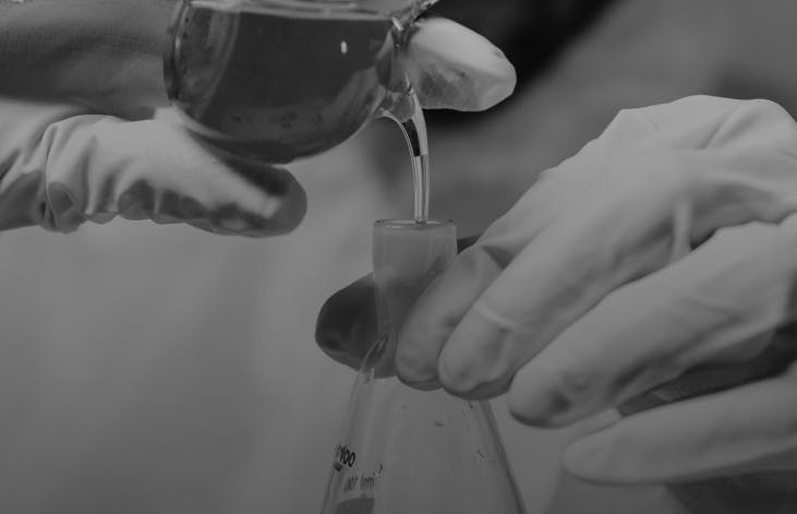 A lab technician wearing gloves and goggles pours cannabis oil into a beaker, highlighting product purity and lab-tested quality.