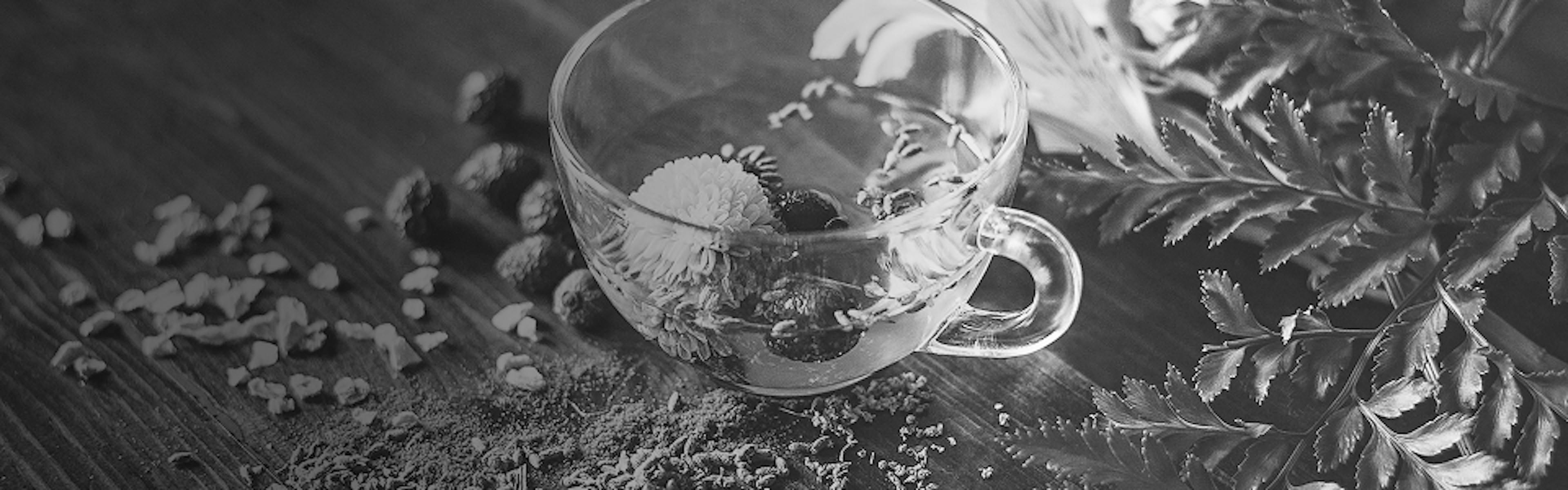 Glass teacup surrounded by loose herbal leaves and blossoms, representing floral and minty terpenes like linalool and humulene