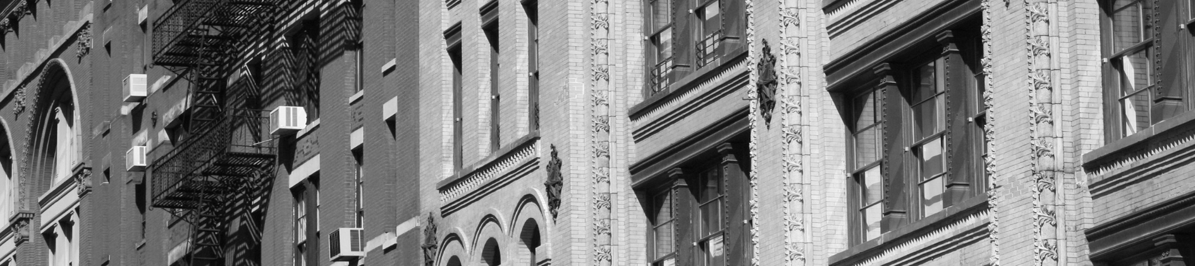 Black and white photo of historic brick and stone building facades in New York City, with decorative molding and tall windows.