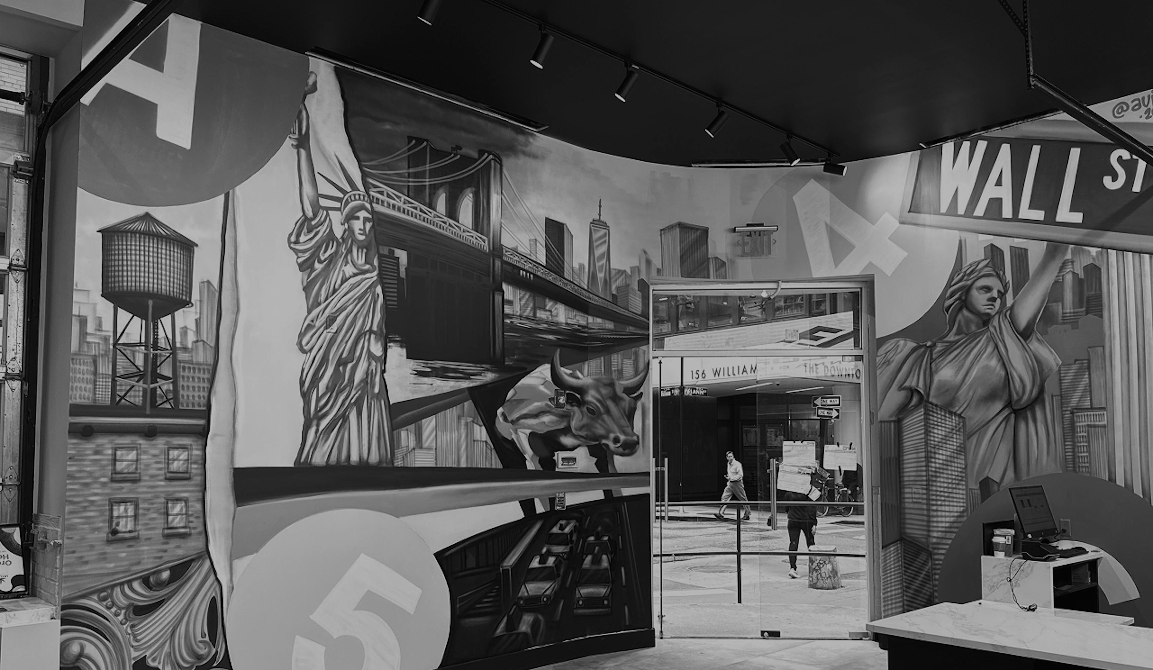 Black-and-white mural of New York City inside a dispensary, featuring large-scale illustrations of the Statue of Liberty, Wall Street sign, Brooklyn Bridge, NYC skyline, water tower, and the Charging Bull. The mural wraps around a corner wall and frames a glass exit door leading to 156 William Street.