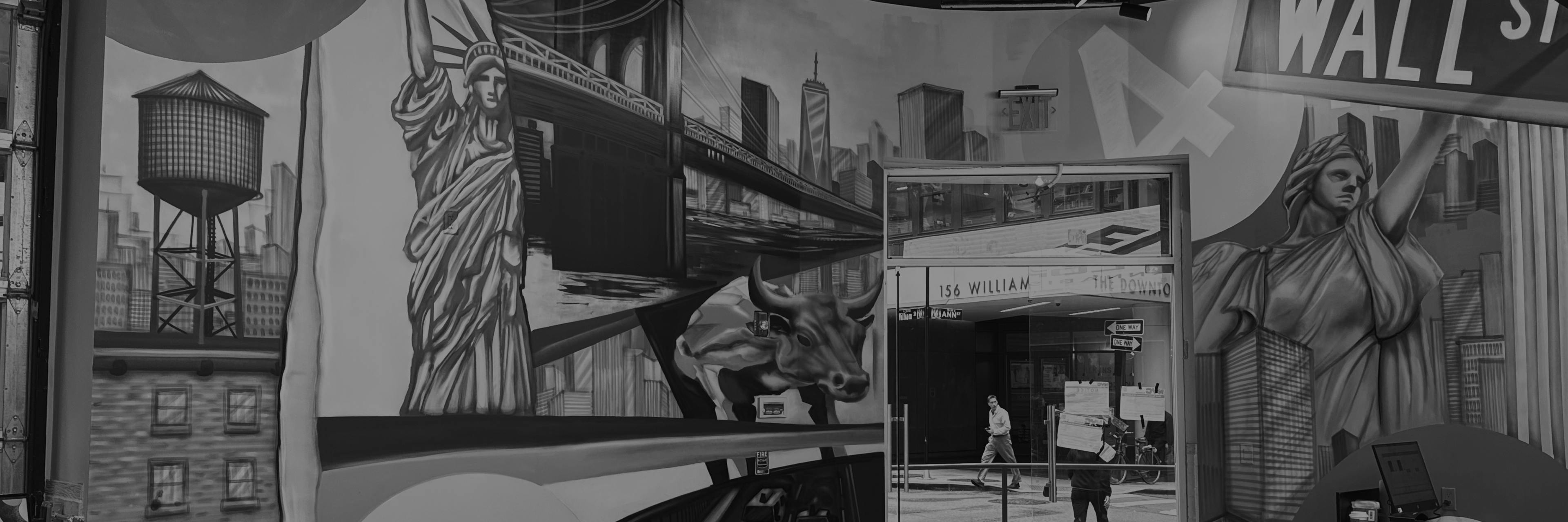 Black-and-white mural of New York City inside a dispensary, featuring large-scale illustrations of the Statue of Liberty, Wall Street sign, Brooklyn Bridge, NYC skyline, water tower, and the Charging Bull. The mural wraps around a corner wall and frames a glass exit door leading to 156 William Street.