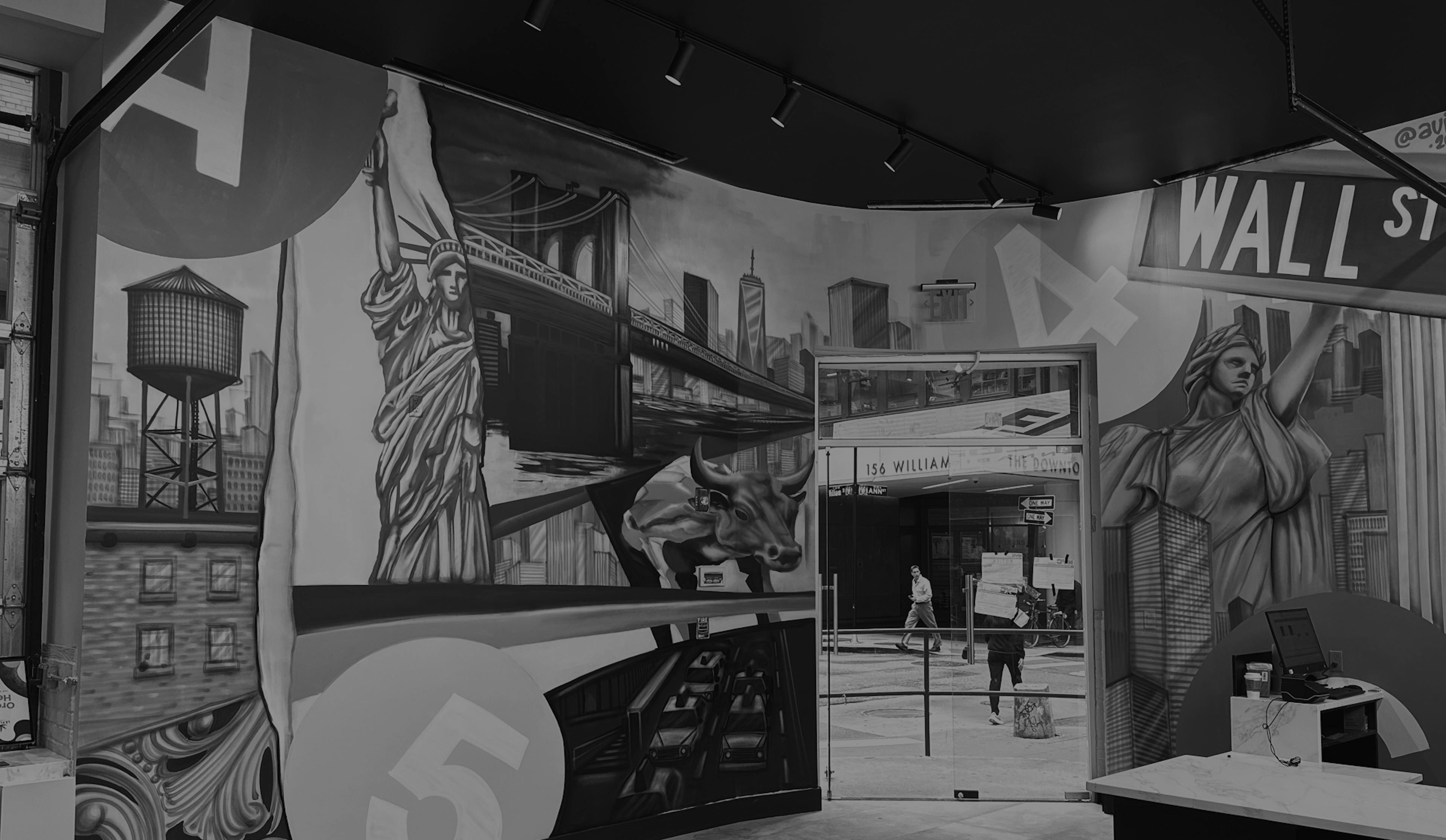 Black-and-white mural of New York City inside a dispensary, featuring large-scale illustrations of the Statue of Liberty, Wall Street sign, Brooklyn Bridge, NYC skyline, water tower, and the Charging Bull. The mural wraps around a corner wall and frames a glass exit door leading to 156 William Street.