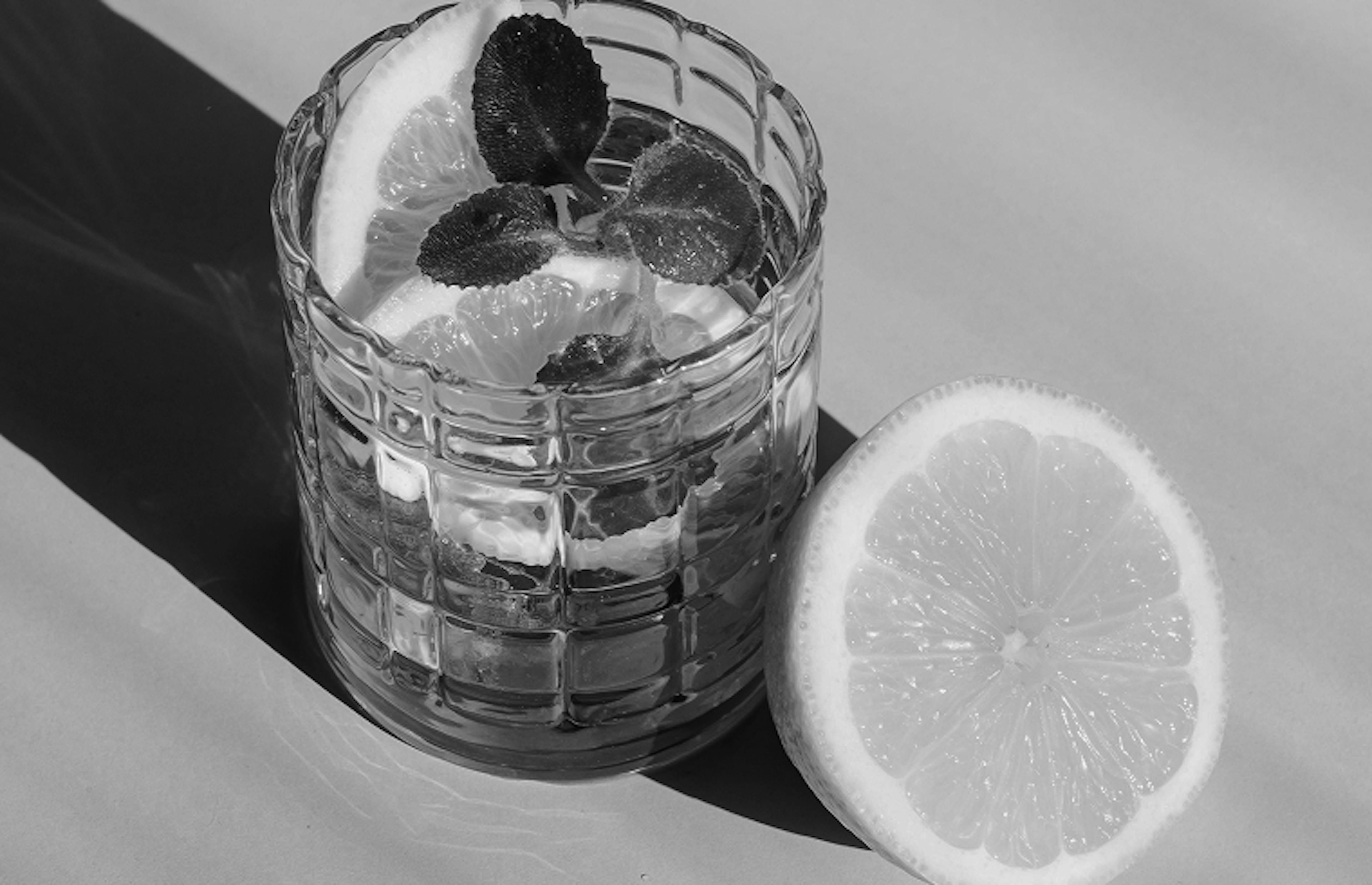 Glass of lemon water with fresh mint leaves next to a halved lemon on a light background.