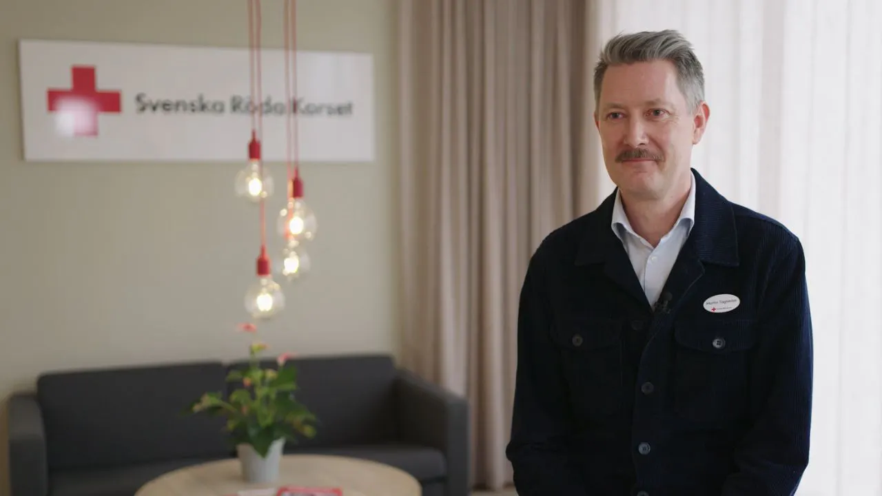 Man med grått hår och mustasch i blå cardigan och ljus skjorta.