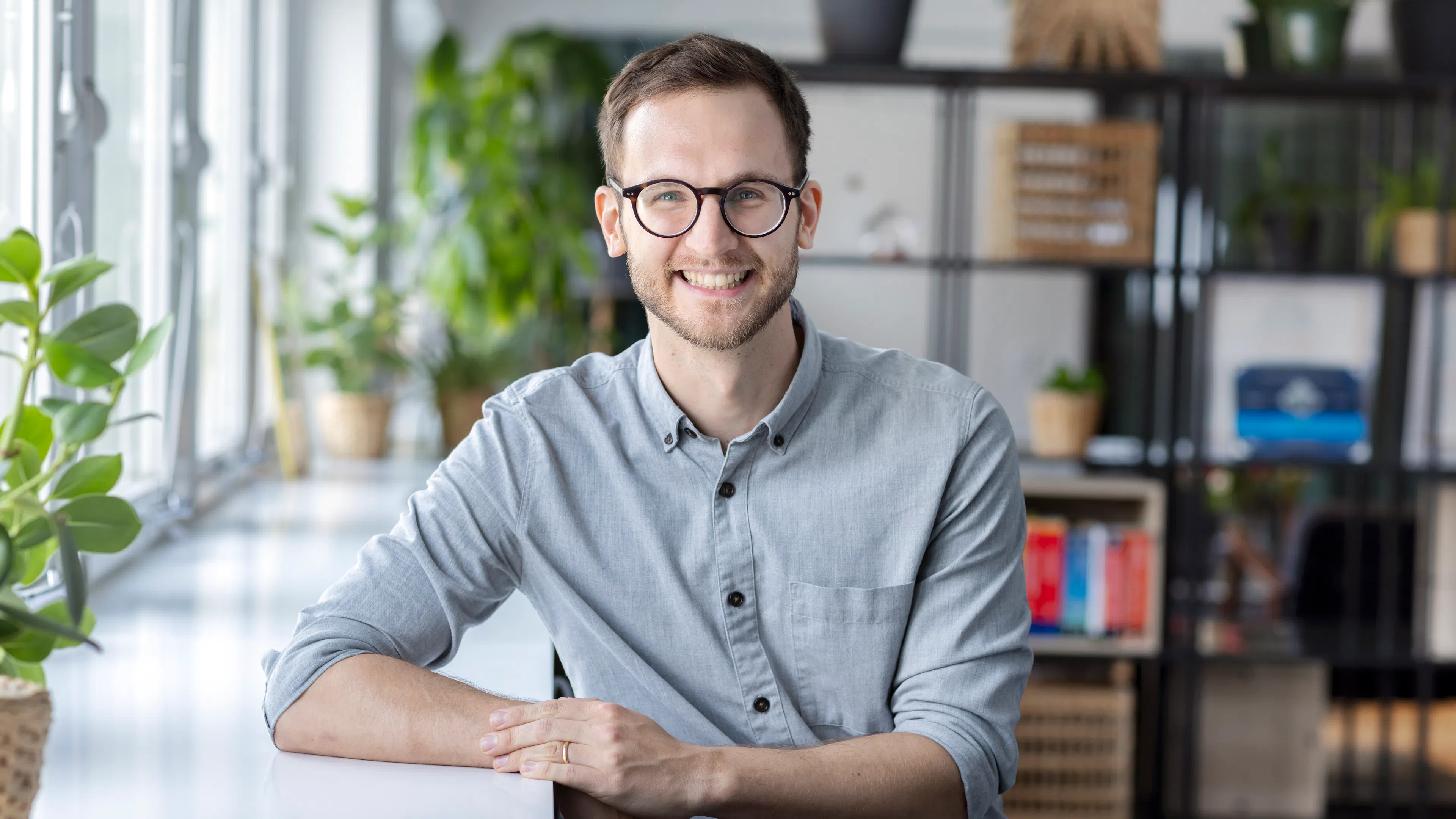 Ein Mann mit Brille und hellgrauem Hemd lehnt sich an eine weiße Kante.