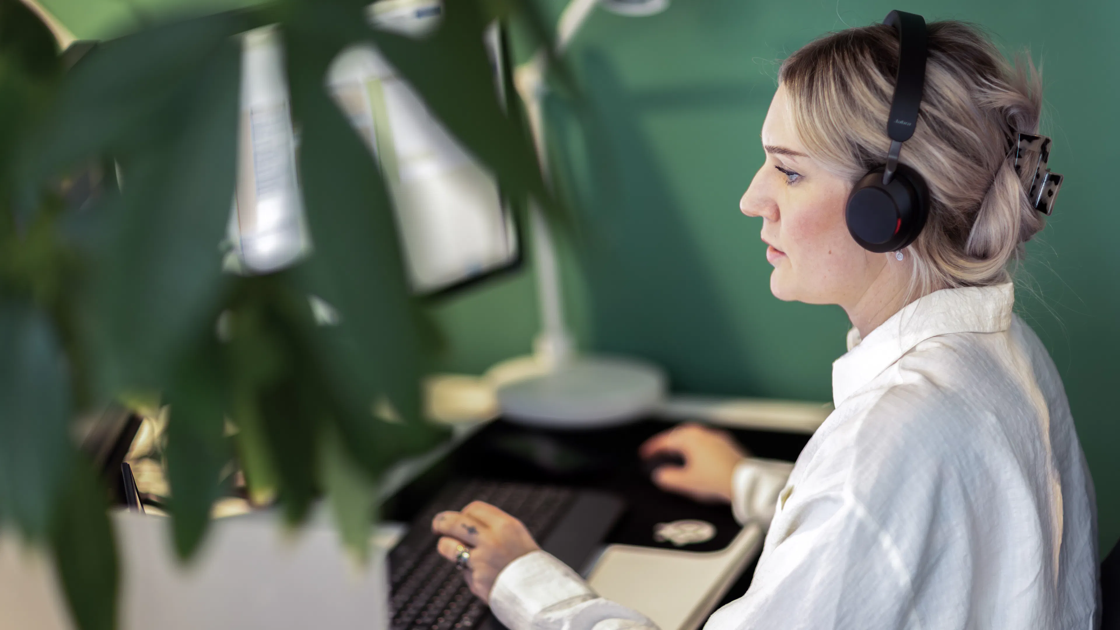 Kvinna i vit skjorta och headset sitter framför en dator.