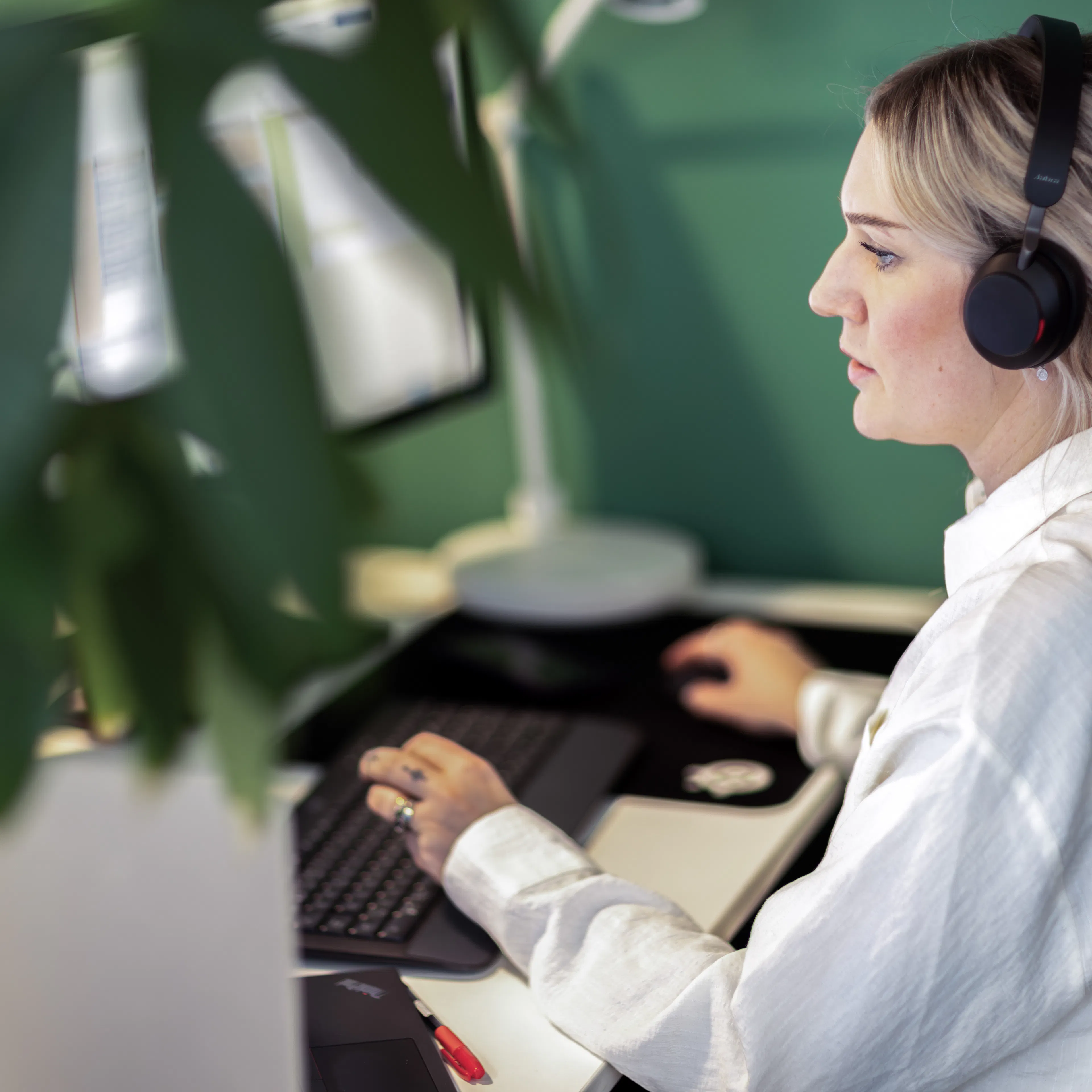 Kvinna i vit skjorta och headset sitter framför en dator.