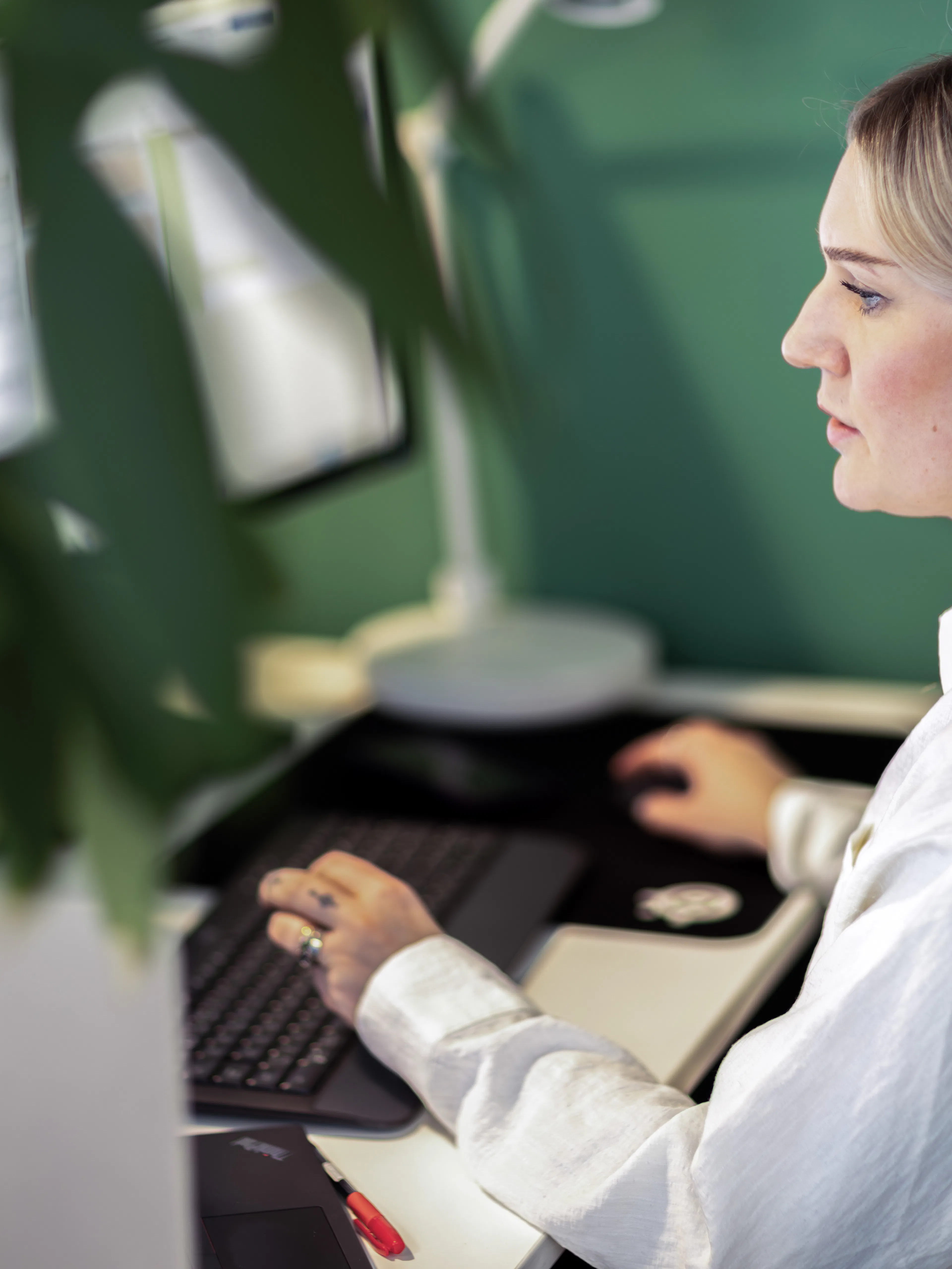 Kvinna i vit skjorta och headset sitter framför en dator.