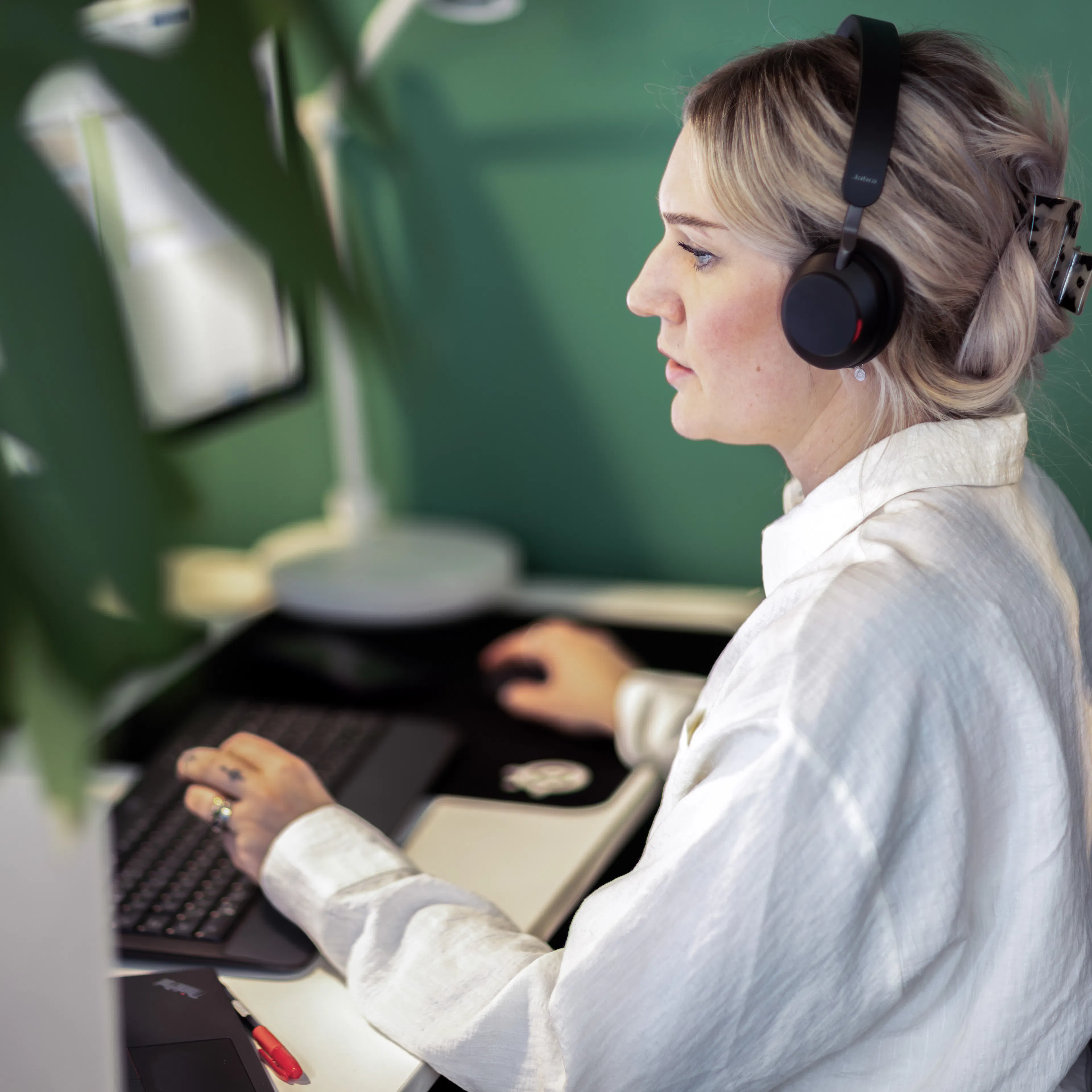 Kvinna i vit skjorta och headset sitter framför en dator.